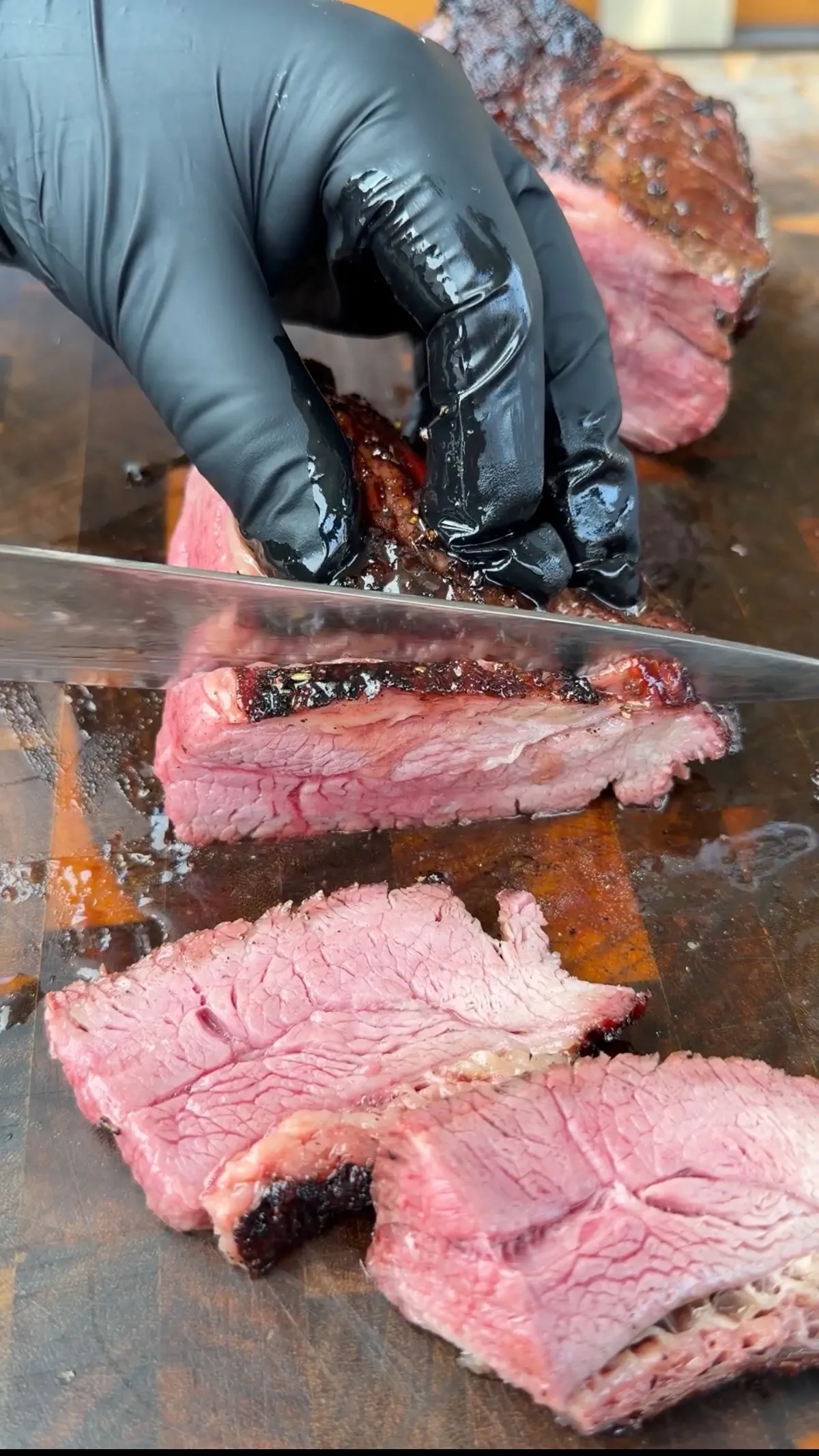 Gloved hands slicing reverse-seared smoked tri-tip against the grain, showing pink smoke ring and dark bark crust