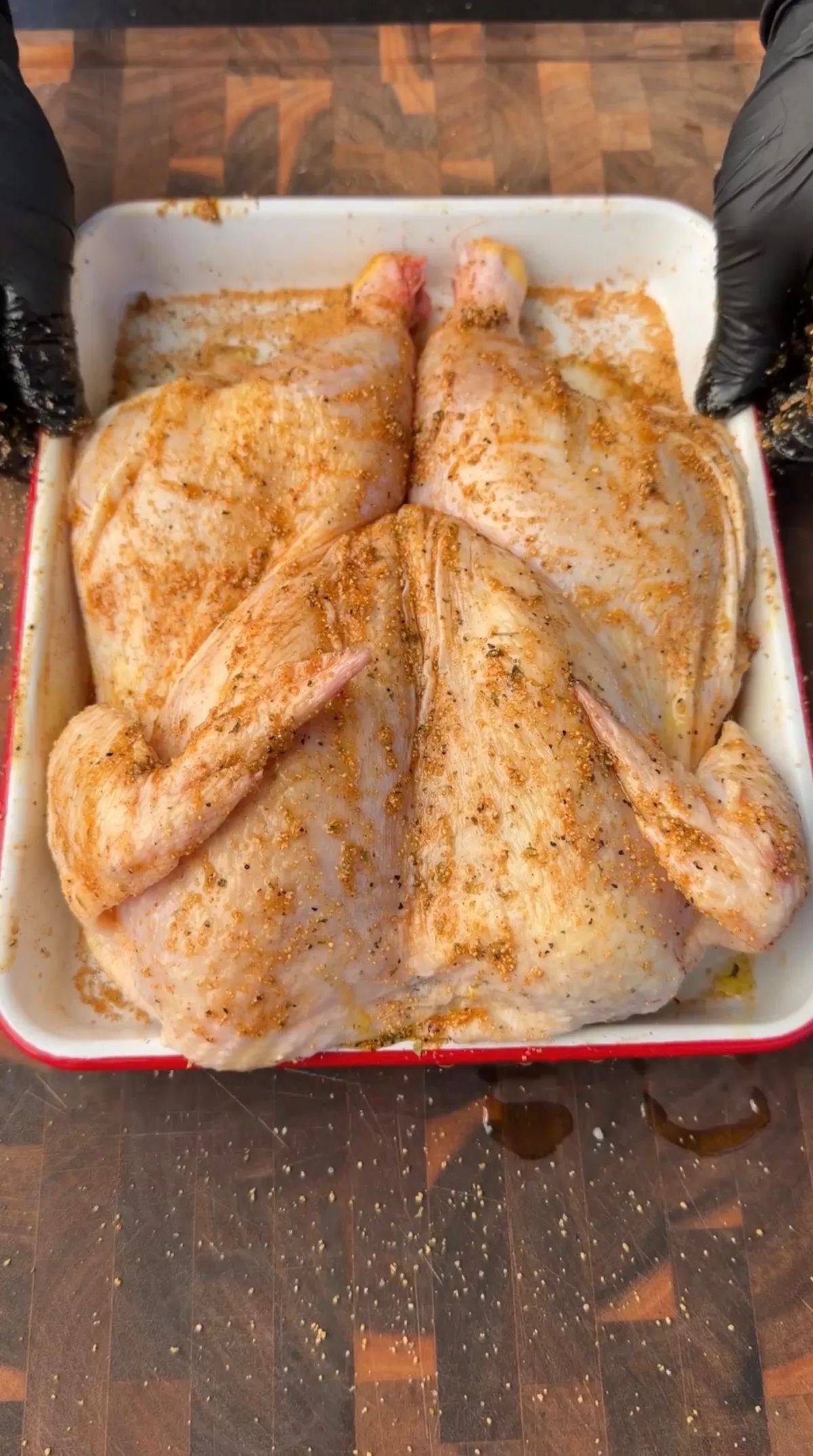 Raw spatchcocked whole chicken rubbed with olive oil and poultry seasoning in a white roasting pan
