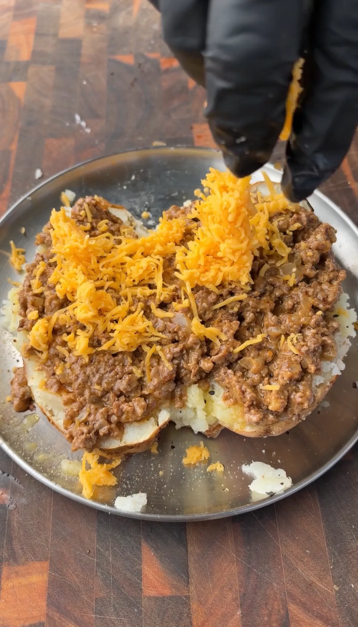 Taco loaded baked potatoes topped with seasoned ground beef and freshly grated cheddar cheese being added by gloved hands