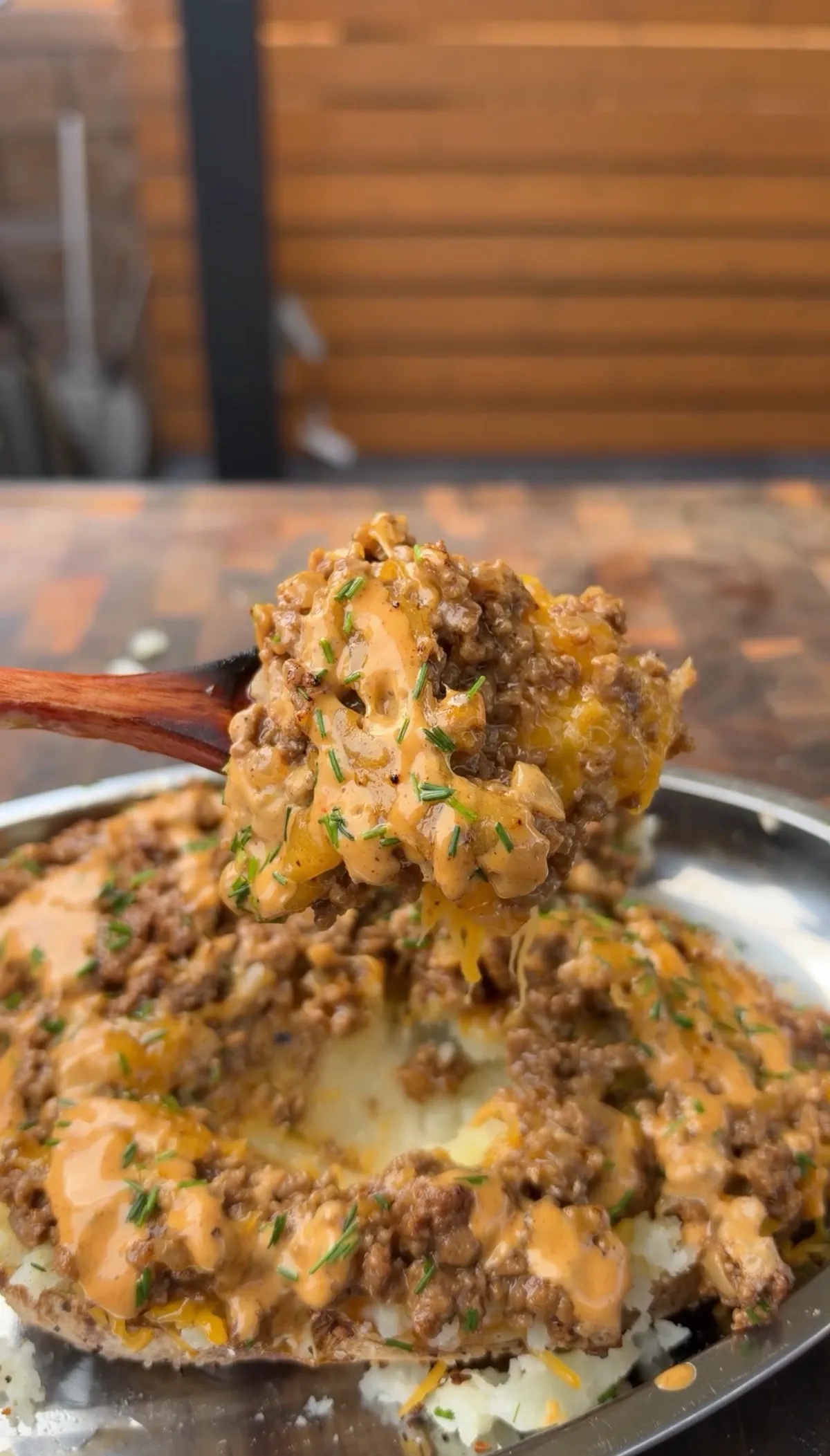 Spoonful of taco beef with nacho cheese lifted over a loaded russet potato half garnished with chives