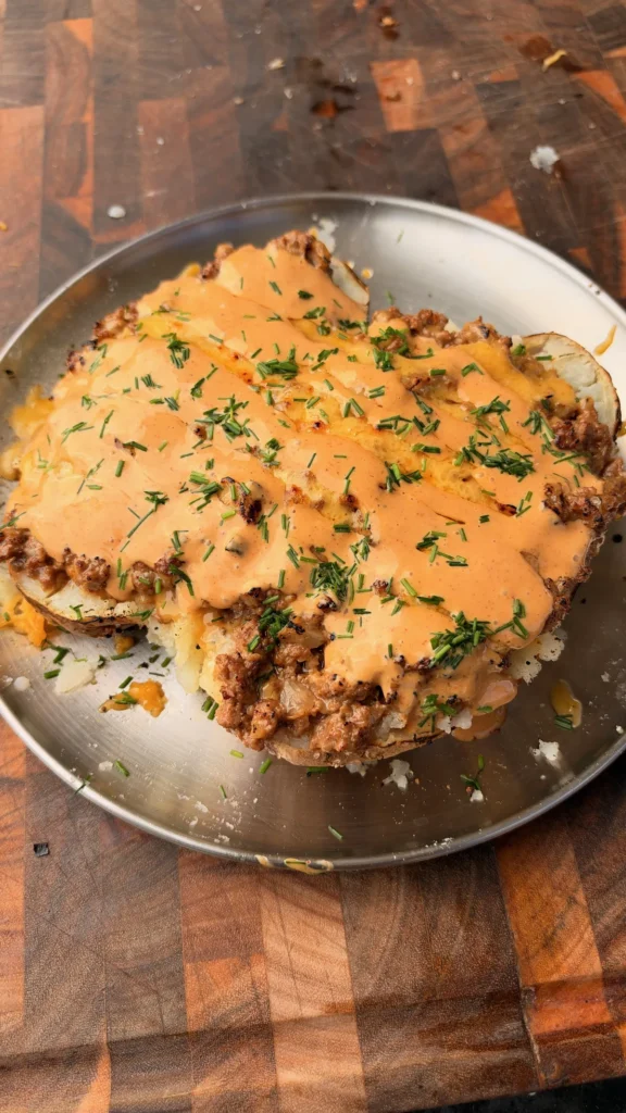 Taco loaded baked potato topped with seasoned ground beef, nacho cheese, chipotle sauce, and fresh chives on a metal plate