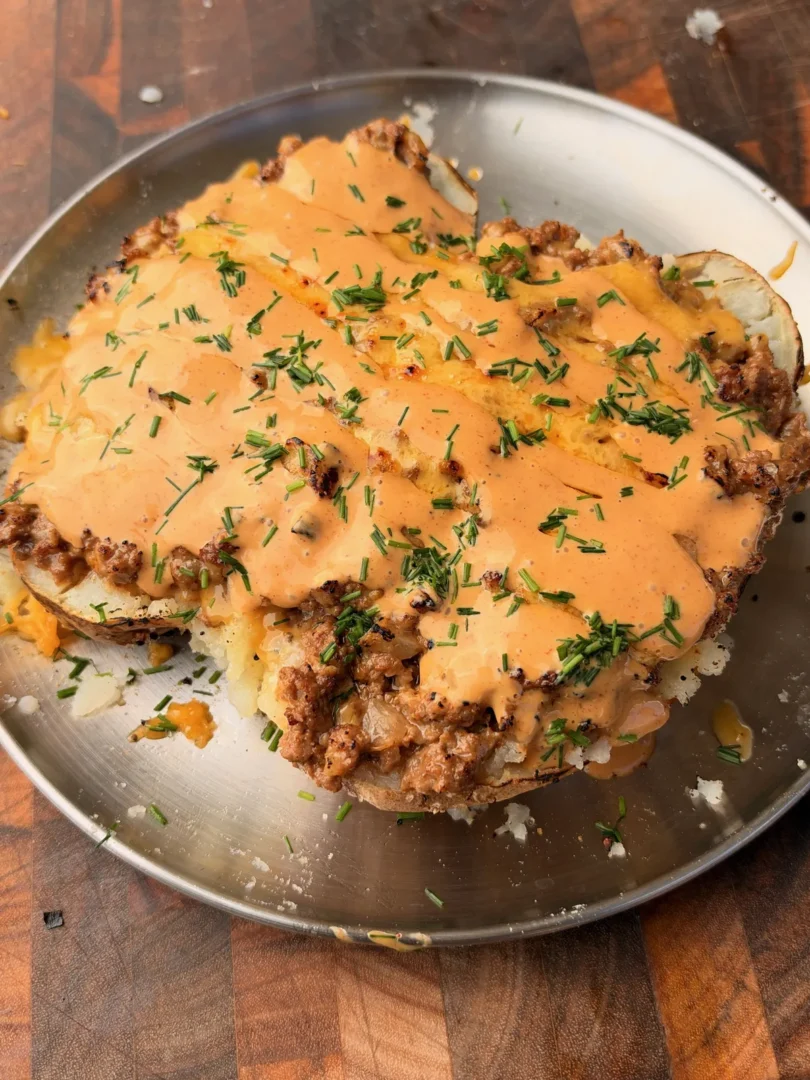 Taco loaded baked potato topped with seasoned ground beef, nacho cheese, chipotle sauce, and fresh chives on a metal plate