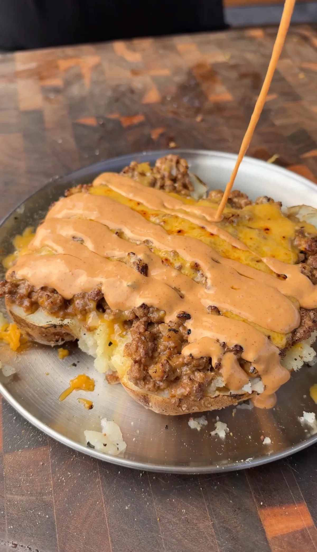 Taco loaded baked potato halves topped with seasoned ground beef, melted cheddar, and chipotle sauce drizzle on a silver plate