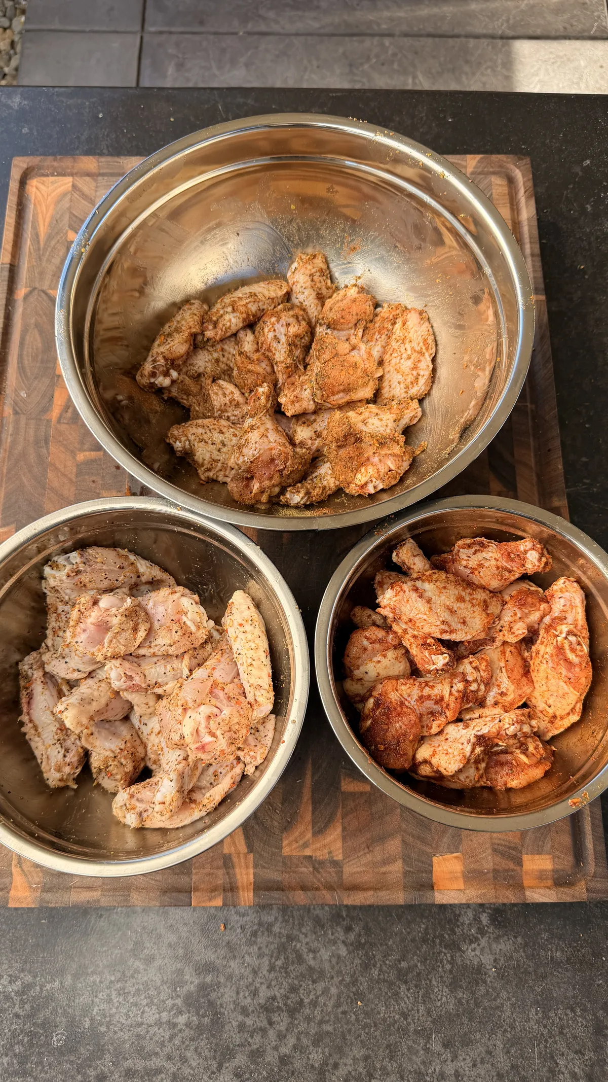 Three bowls of raw chicken wings seasoned with Cajun, lemon pepper, and Dano's Cajun dry rub before grilling