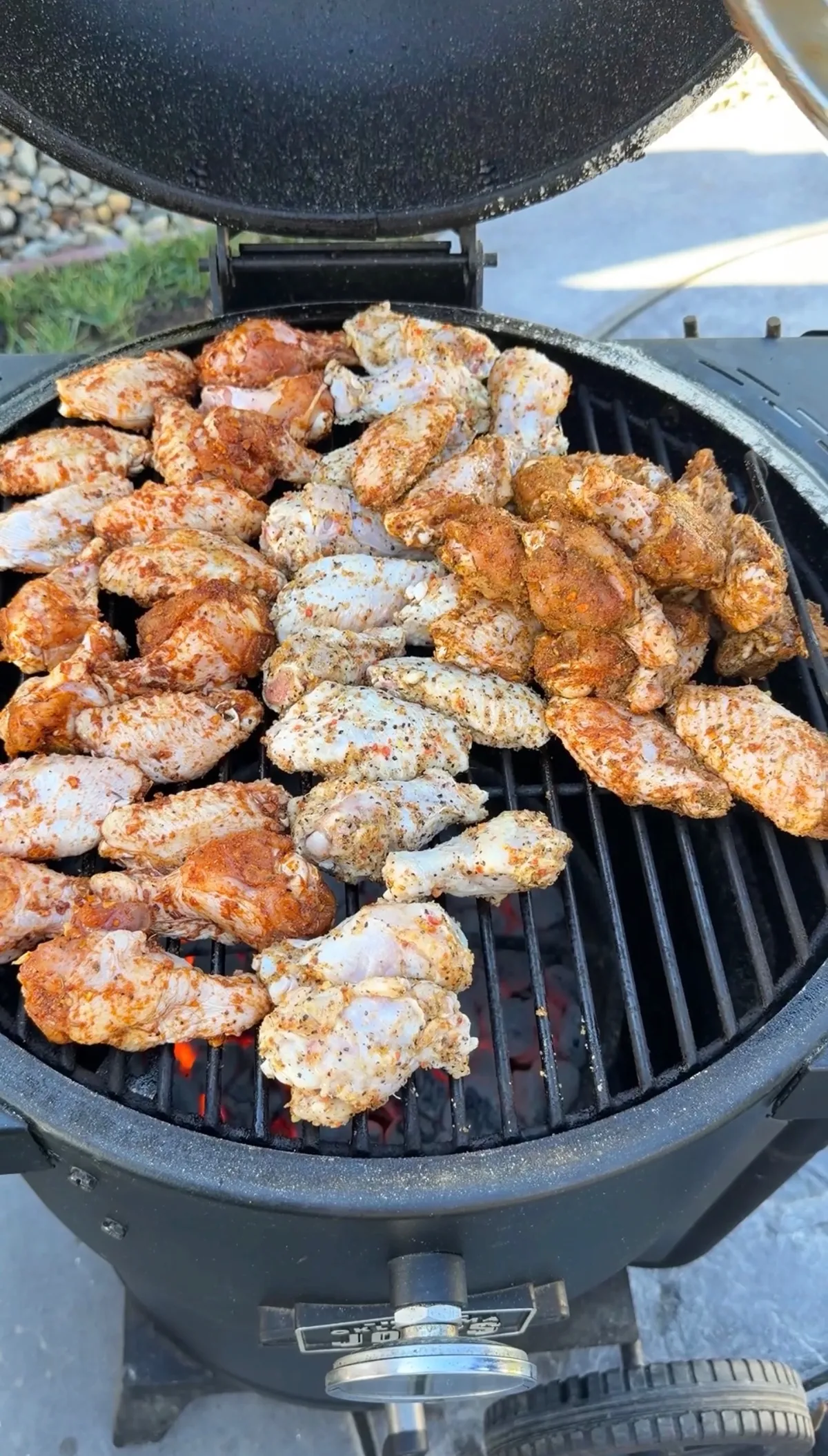 Three-way chicken wings seasoned with Cajun, lemon pepper, and Dano's dry rub grilling on a charcoal grill at 350°F
