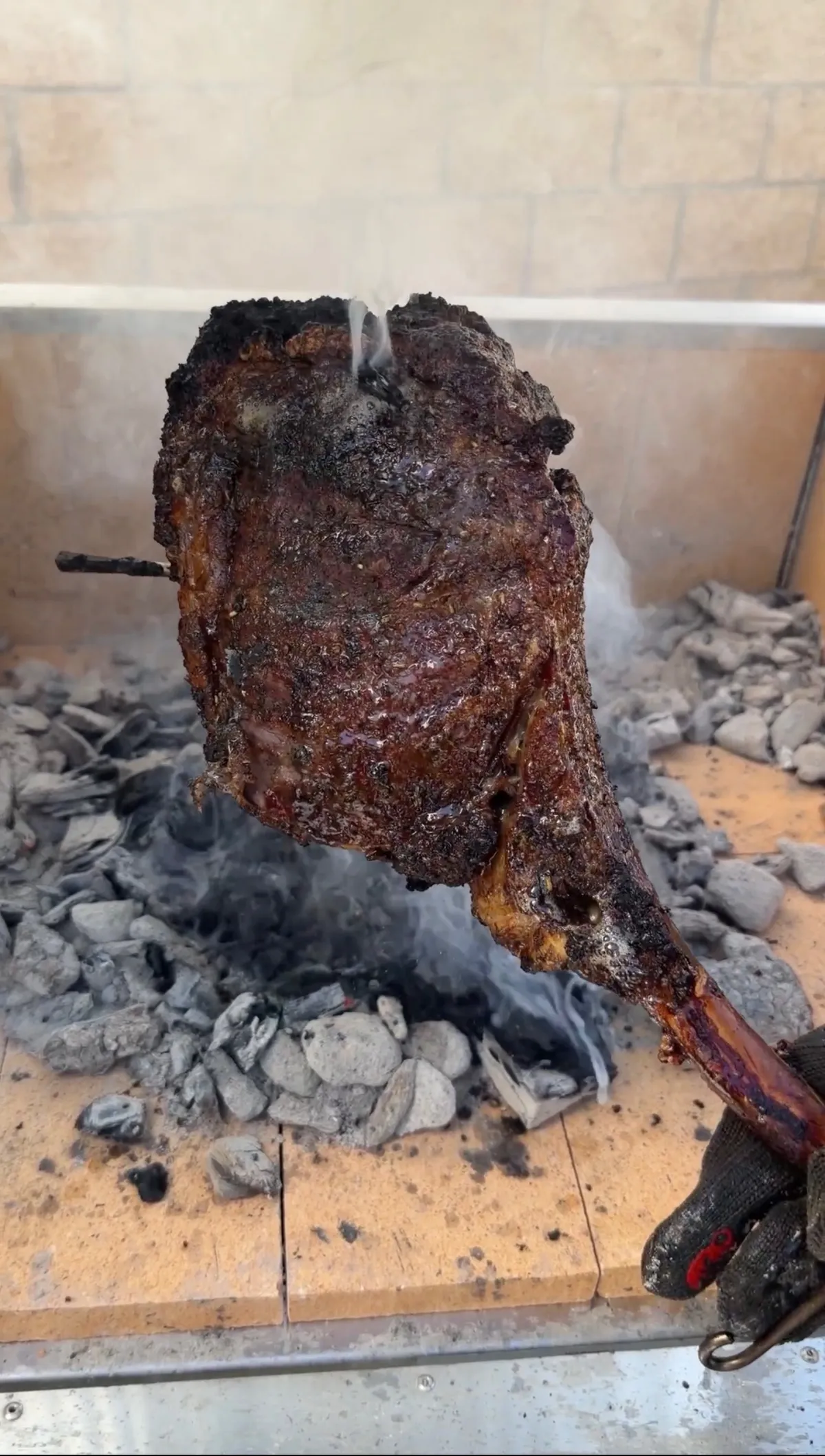 Tomahawk steak caveman-seared directly on lump charcoal with a dark smoky crust, held by a gloved hand
