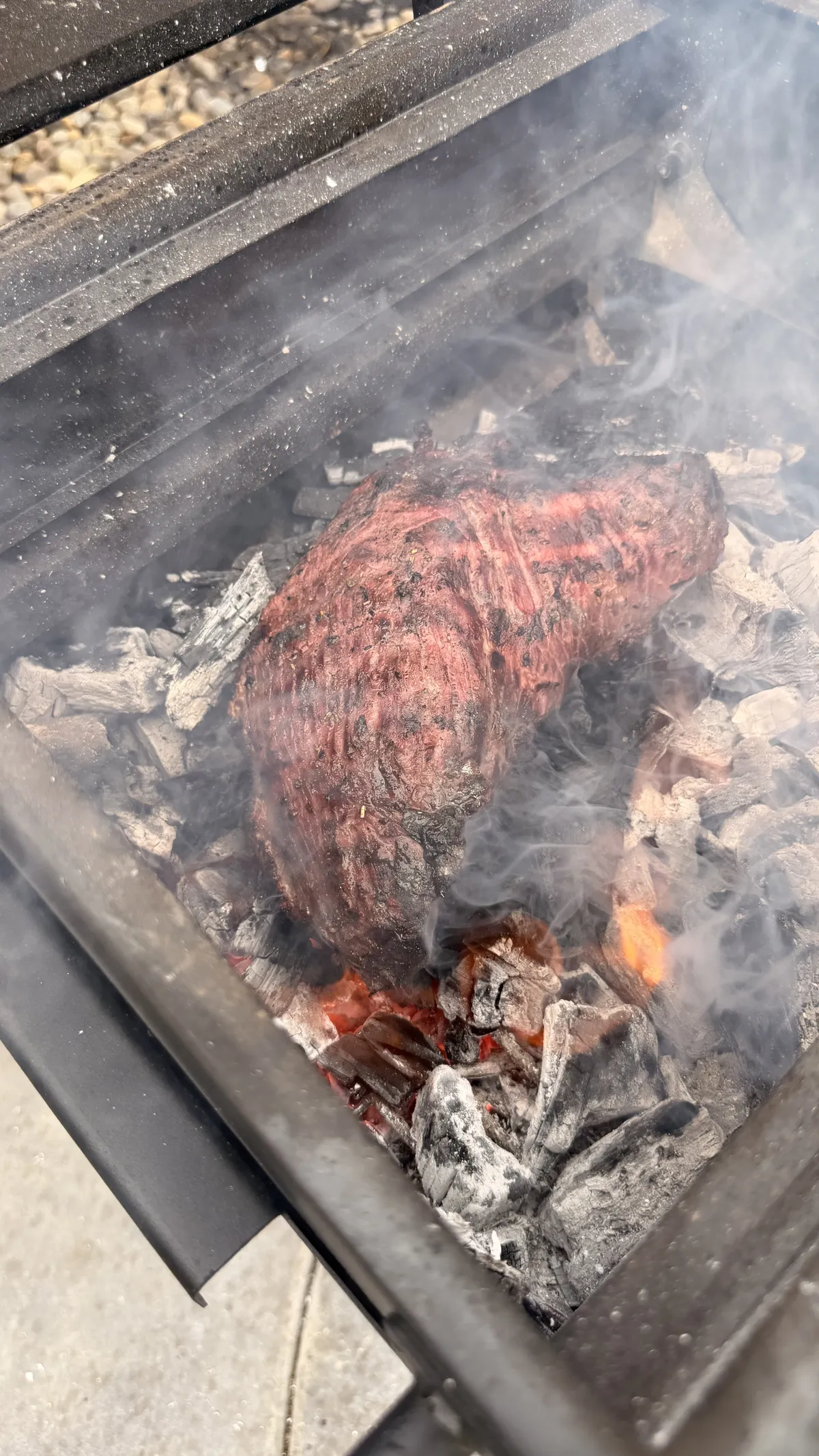 Tri-tip searing directly over hot lump charcoal with smoke rising during Caveman-style reverse sear
