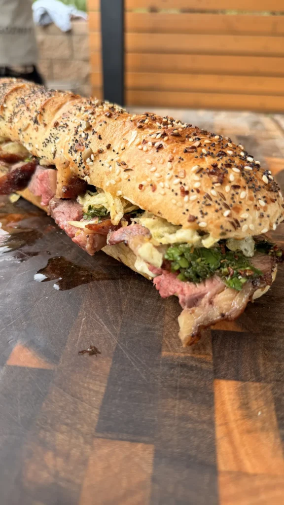 Thinly sliced tri-tip sandwich with garlic aioli, chimichurri, and salted potato chips on a seeded baguette