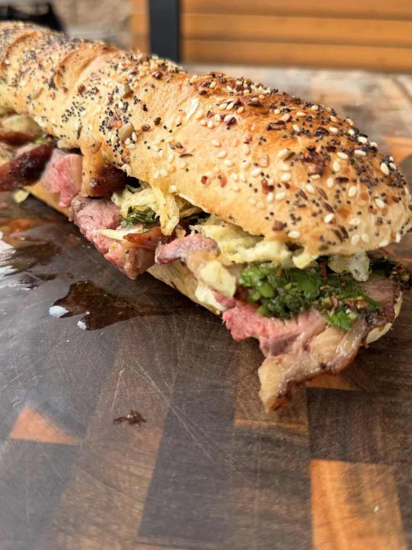 Thinly sliced tri-tip sandwich with garlic aioli, chimichurri, and salted potato chips on a seeded baguette