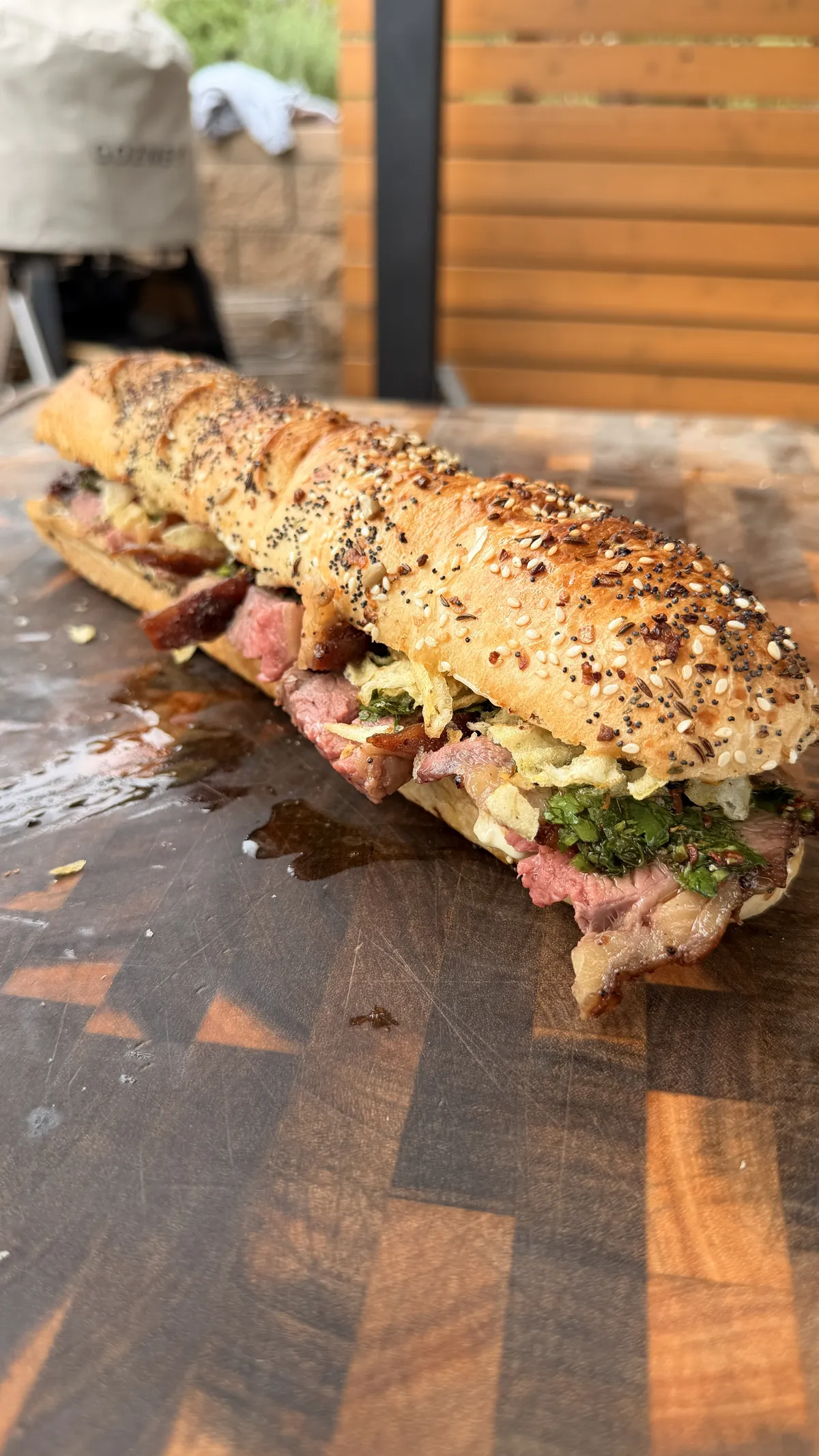 Thinly sliced tri-tip sandwich with garlic aioli, chimichurri, and crispy potato chips on a seeded baguette