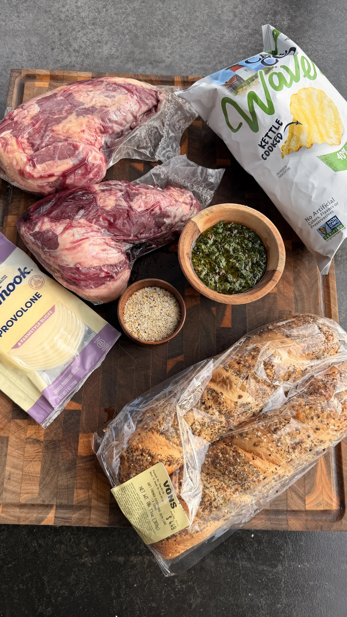 Tri-tip, chimichurri, sourdough loaf, provolone, and kettle-cooked potato chips on a wooden cutting board