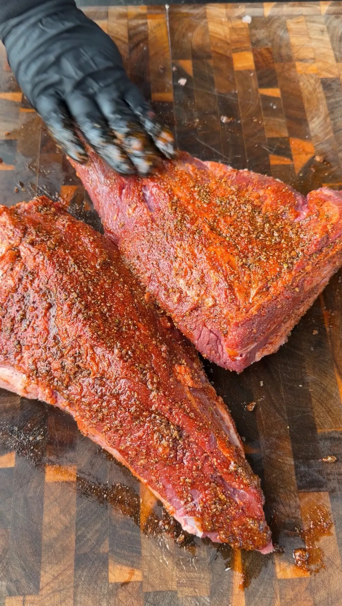 Two raw tri-tips generously coated in olive oil seasoning mud rub on a wooden cutting board