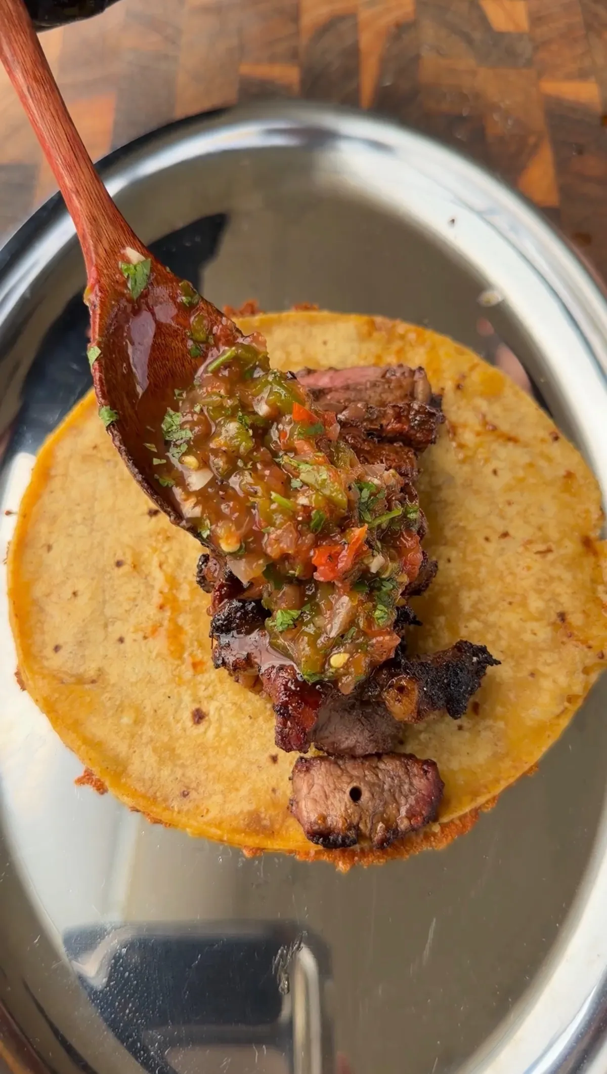 Cheese-crusted corn tortilla topped with grilled tri-tip pieces and a spoonful of roasted salsa on a silver plate