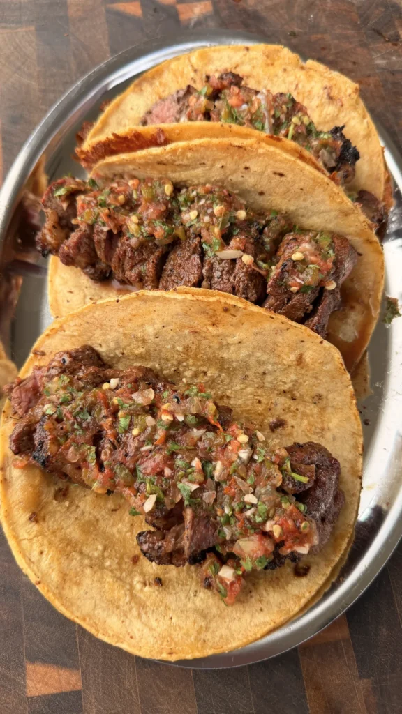 Cheese-crusted corn tortilla tri-tip tacos topped with roasted salsa on a silver tray
