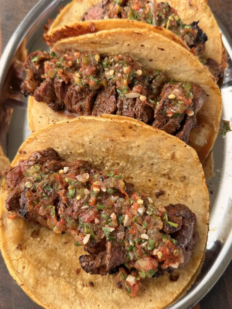 Cheese-crusted corn tortilla tri-tip tacos topped with roasted salsa on a silver tray