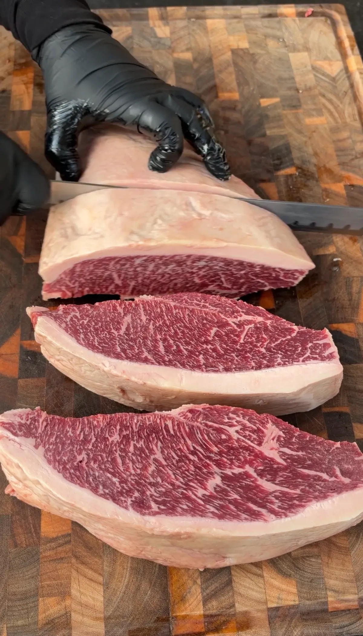 Whole wagyu picanha being sliced against the grain into 1.5-inch steaks on a wooden cutting board
