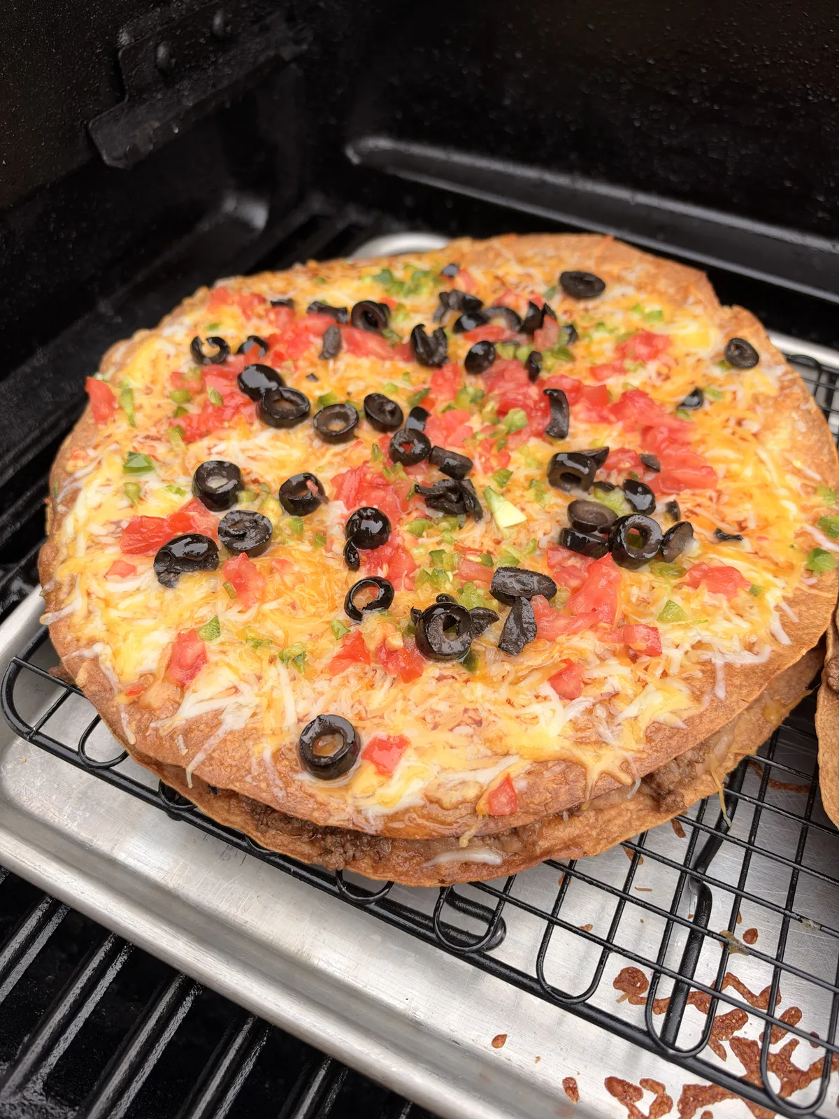 Homemade Taco Bell copycat Mexican pizza on a wire rack with melted Colby Jack cheese, diced tomatoes, sliced black olives, and jalapeños