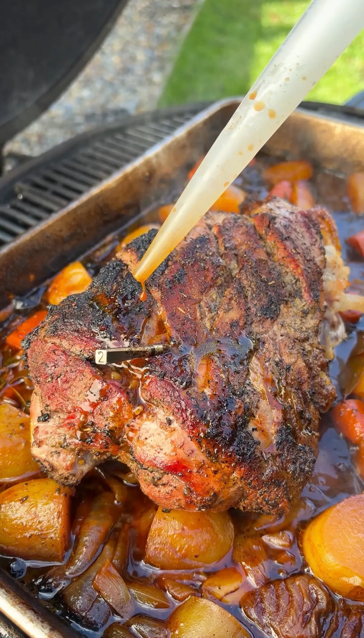 Baster injecting pan juices over fall-apart braised leg of lamb with potatoes, carrots, and onions in roasting tray