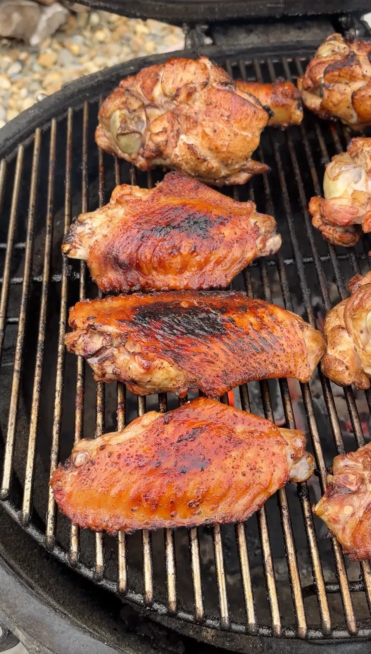 BBQ-glazed turkey wing flats and drums caramelizing on charcoal grill grates with tacky, darkened sauce