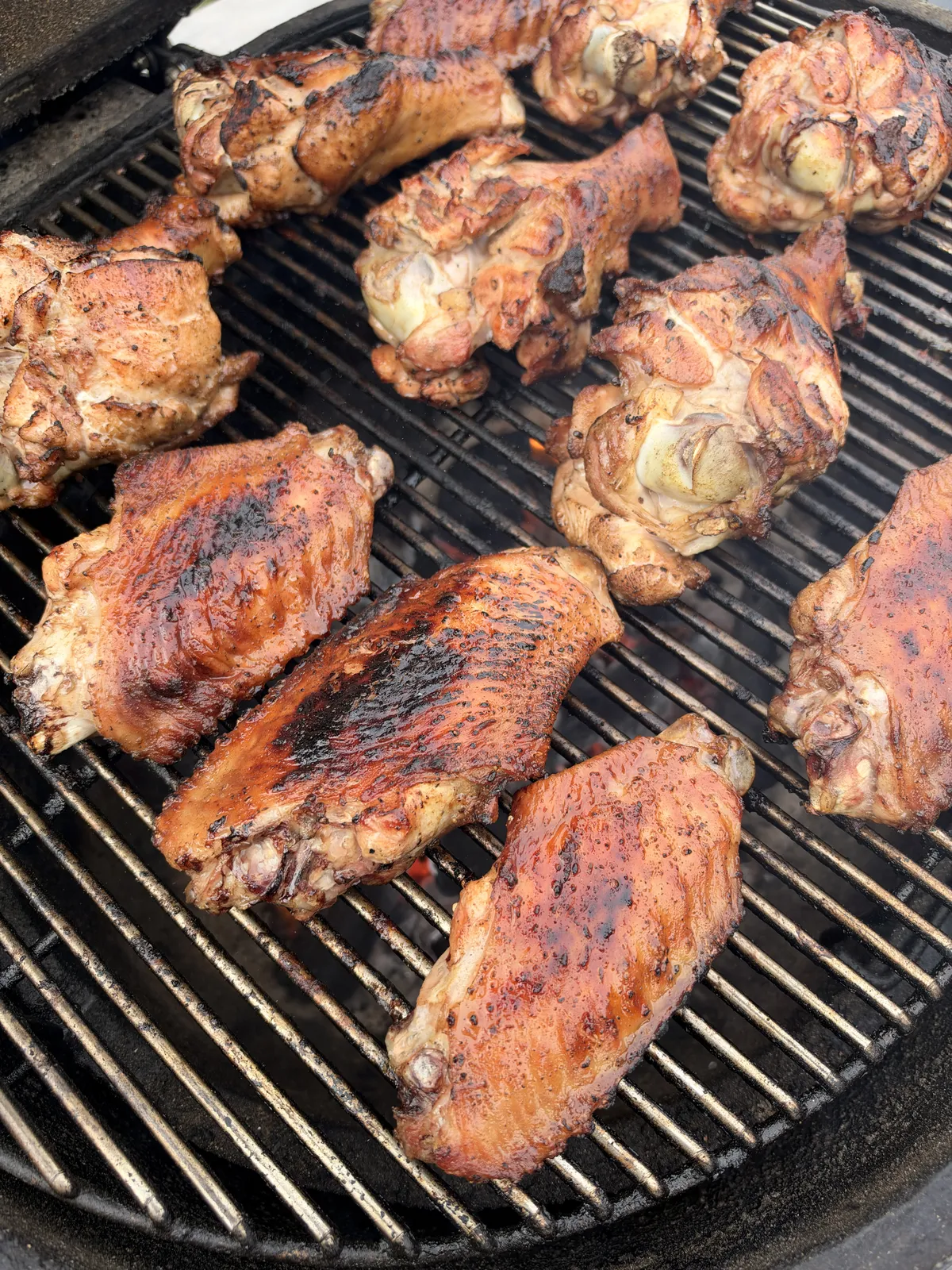 Turkey wing flats and drums coated in caramelized BBQ sauce grilling on a charcoal grate at 350°F