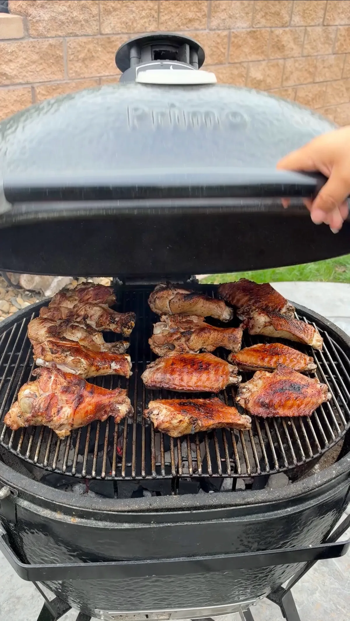 Lid being lifted on a Primo ceramic grill revealing 12 grilled BBQ turkey wing flats and drums cooking on the grates
