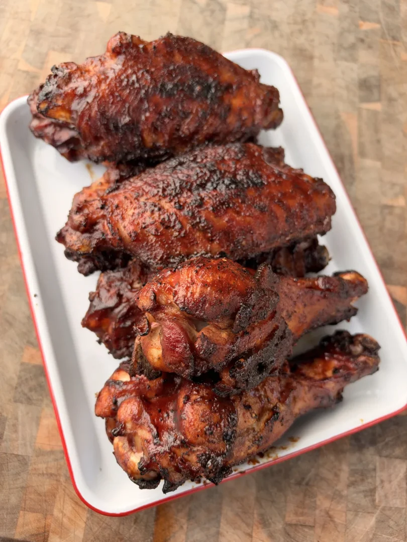 Grilled BBQ turkey wing drums and flats with caramelized glaze piled on a white enamel serving tray