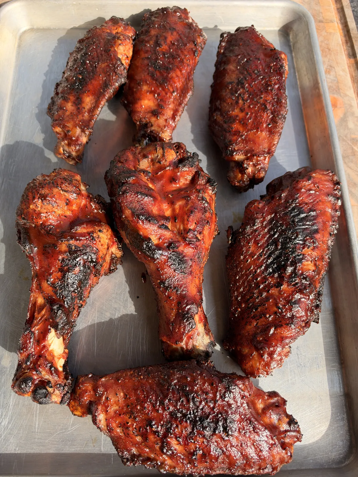 Seven grilled BBQ turkey wing pieces with caramelized sauce resting on a metal sheet pan