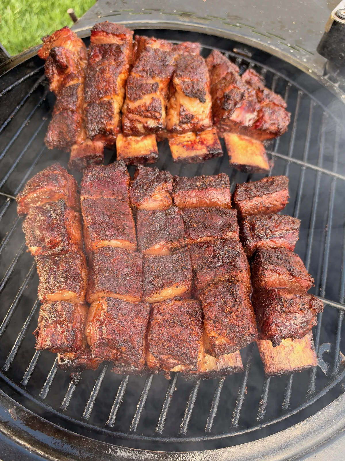 Smoked beef short rib burnt end cubes arranged upright on a round charcoal grill grate with deep bark crust