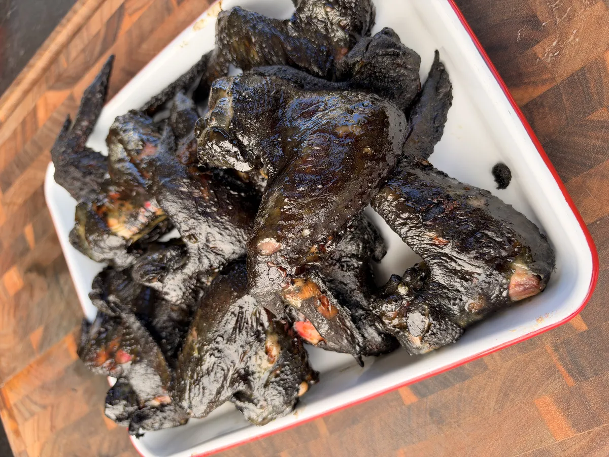 Grilled black chicken bat wings coated in soy-honey-chili marinade piled in a white enamel tray on a wood cutting board
