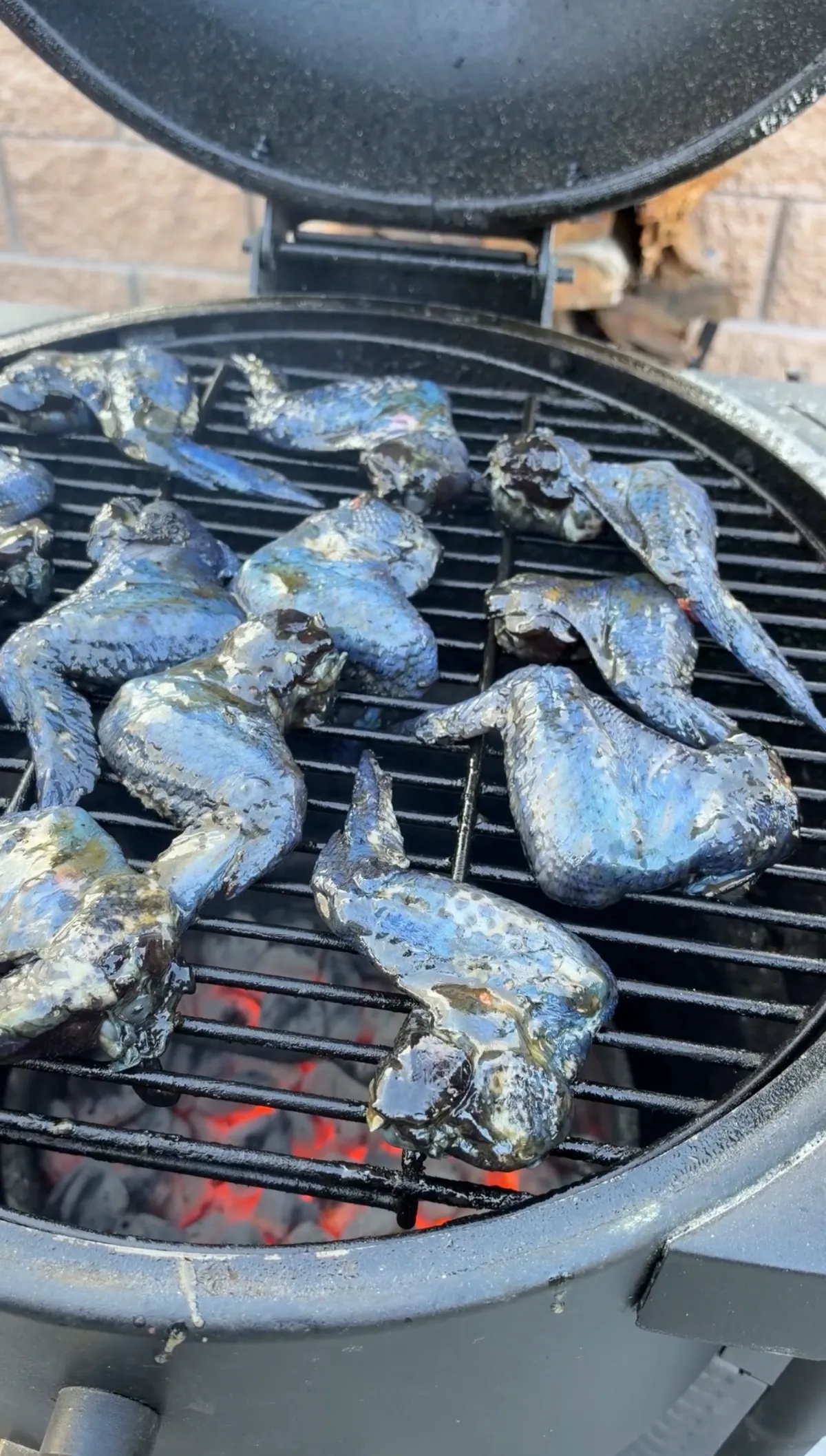Black marinated chicken wings grilling over hot charcoal on a kamado-style grill, showing deep black color from soy-honey-chili marinade