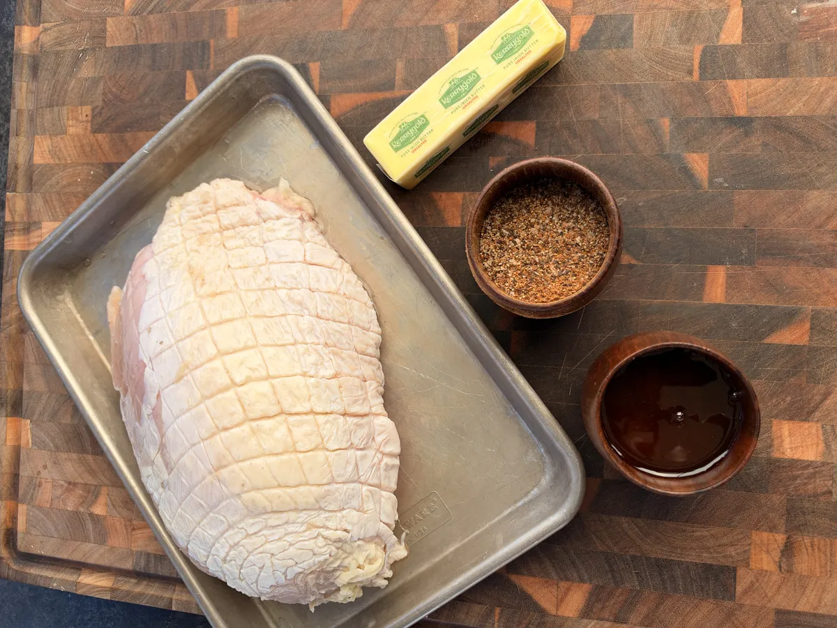 Raw boneless turkey breast on sheet pan with Kerrygold butter, salt-pepper-garlic rub, and honey in wooden bowls