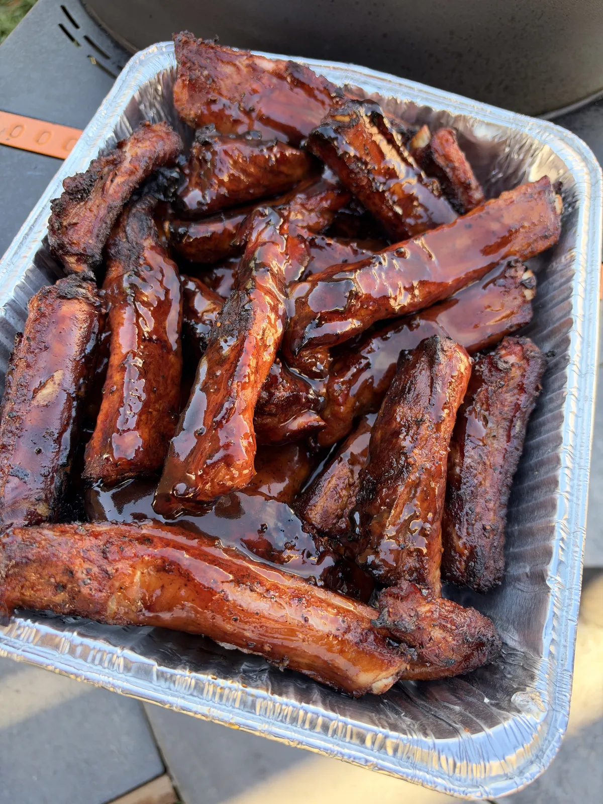 Individual St. Louis-style pork party ribs coated in glossy sticky barbecue sauce with honey and brown sugar in a foil tray
