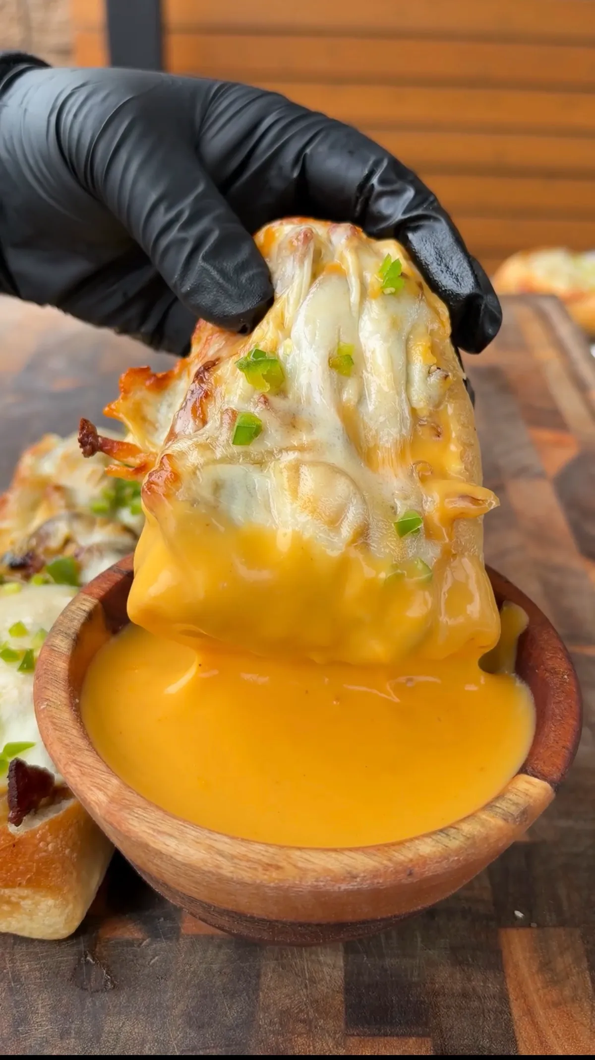 Cheesesteak stuffed bread boat being dipped into warm nacho cheese sauce in a wooden bowl, topped with melted provolone