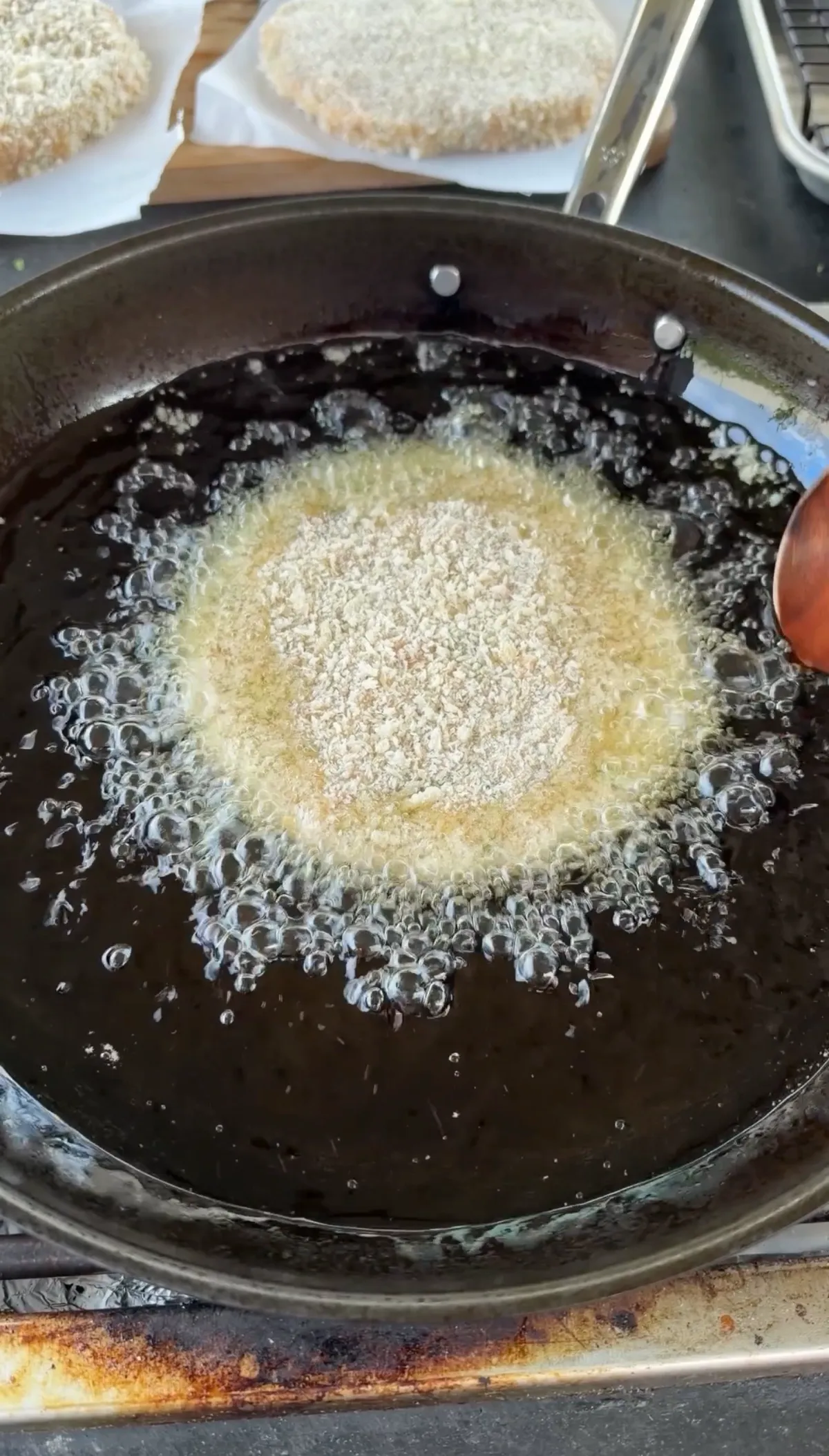 Panko-breaded shrimp burger patty sizzling in 350°F neutral frying oil in a shallow pan