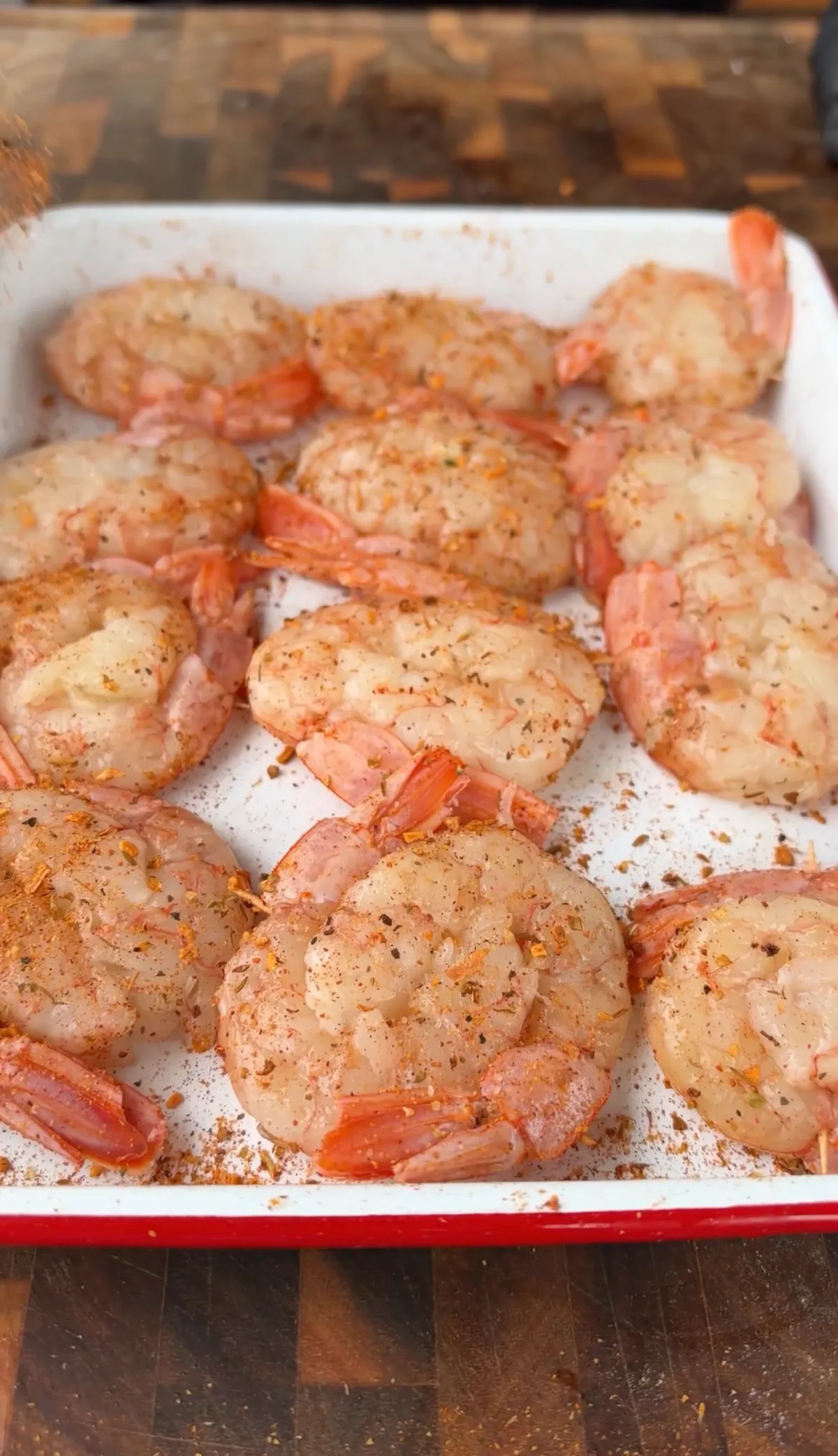 Large raw shrimp seasoned with Cajun seasoning arranged in a white enamel baking dish, ready to be breaded and fried
