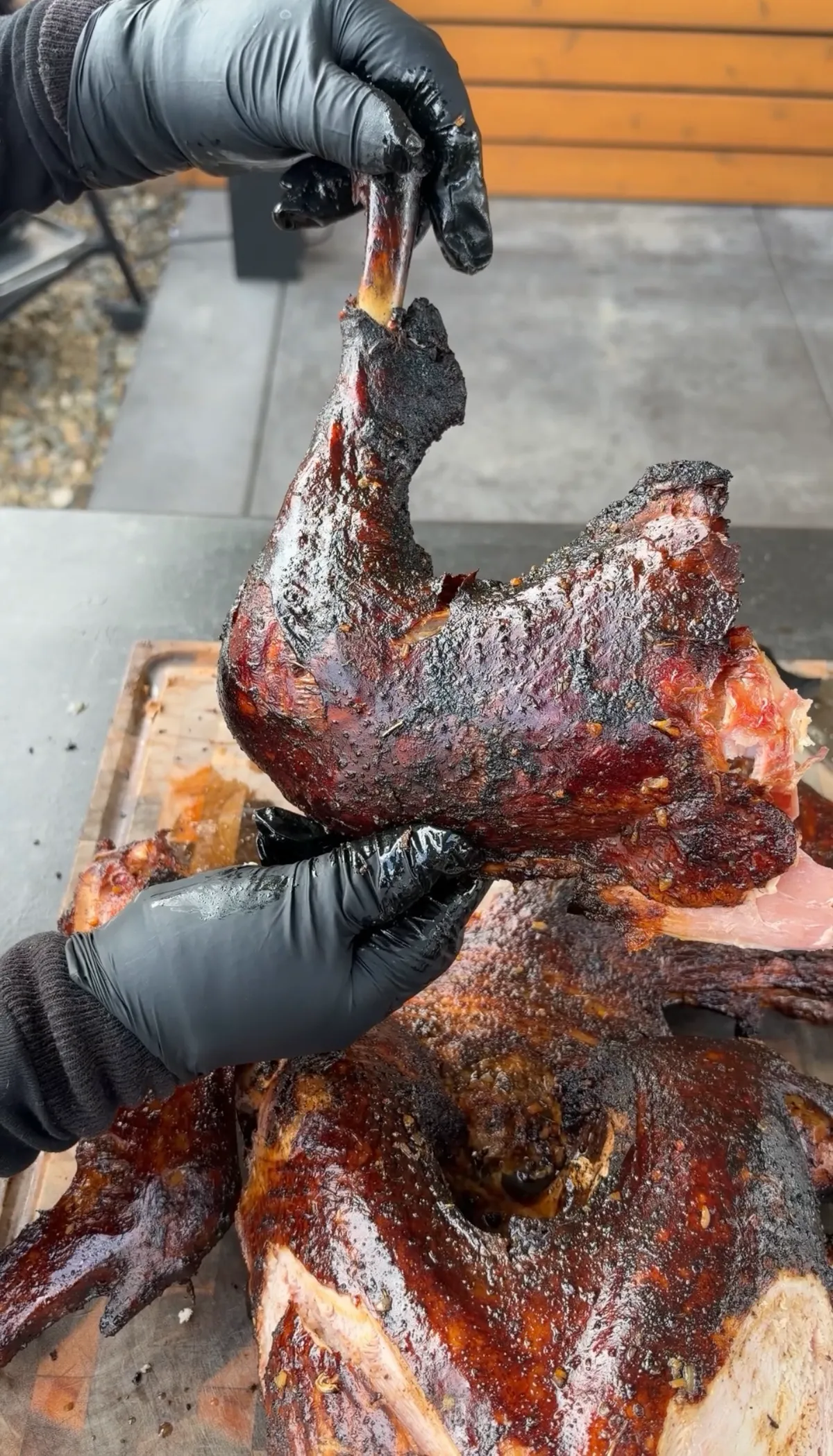 Gloved hands pulling a smoked Cajun turkey leg from a frog-style carved turkey with dark bark crust