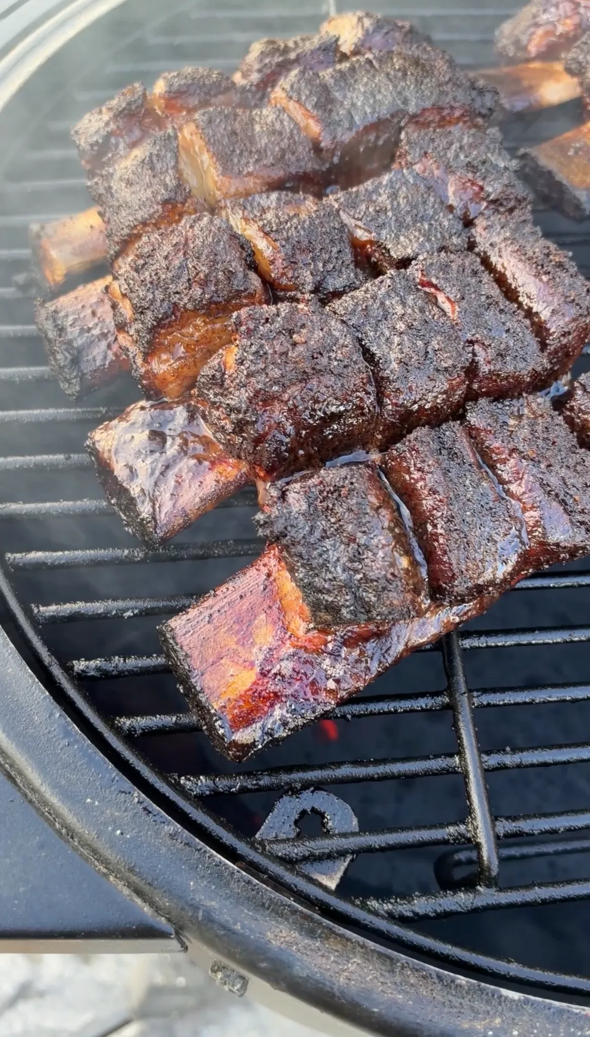 Deeply caramelized beef short rib burnt ends with dark bark piled on a round charcoal grill grate