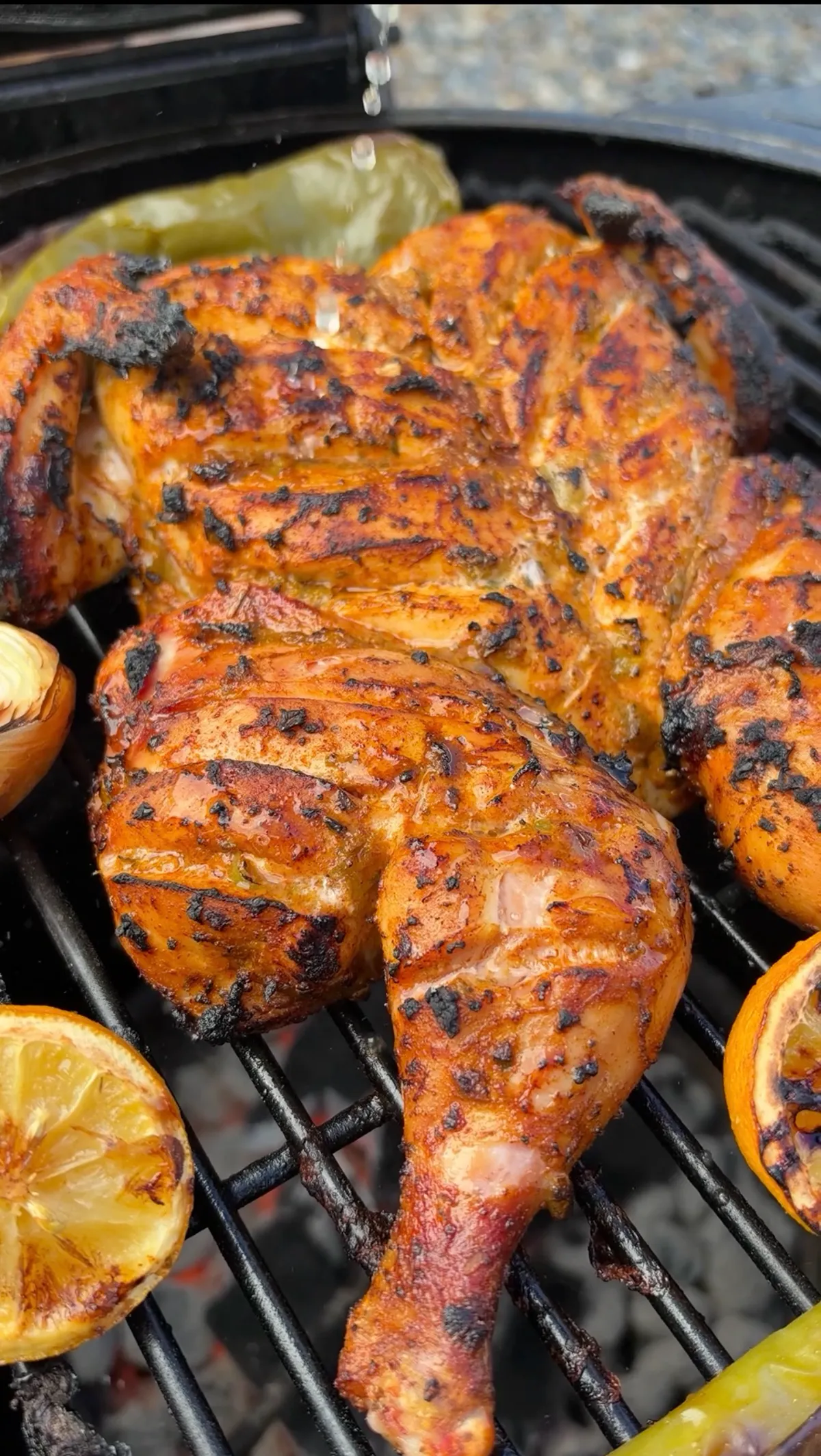 Spatchcocked green chile lime chicken on charcoal grill with charred lemon halves and grilled Anaheim peppers