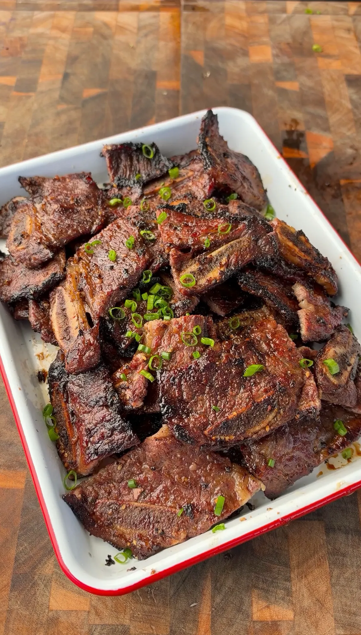 Grilled Korean Kalbi flanken-cut beef short ribs piled in white enamel dish, garnished with sliced green onions