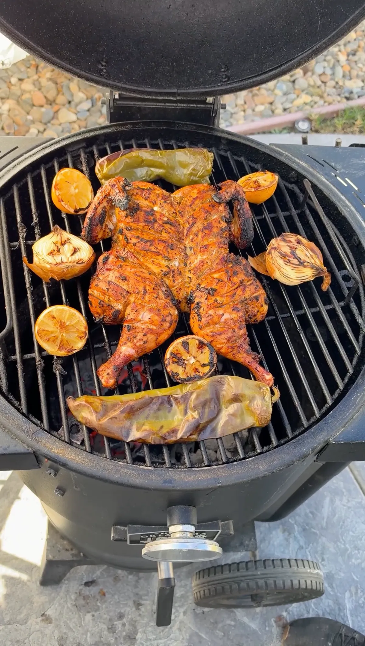 Spatchcocked green chile lime chicken grilling at 350°F with charred lemon halves, Anaheim peppers, and onions on a kamado grill