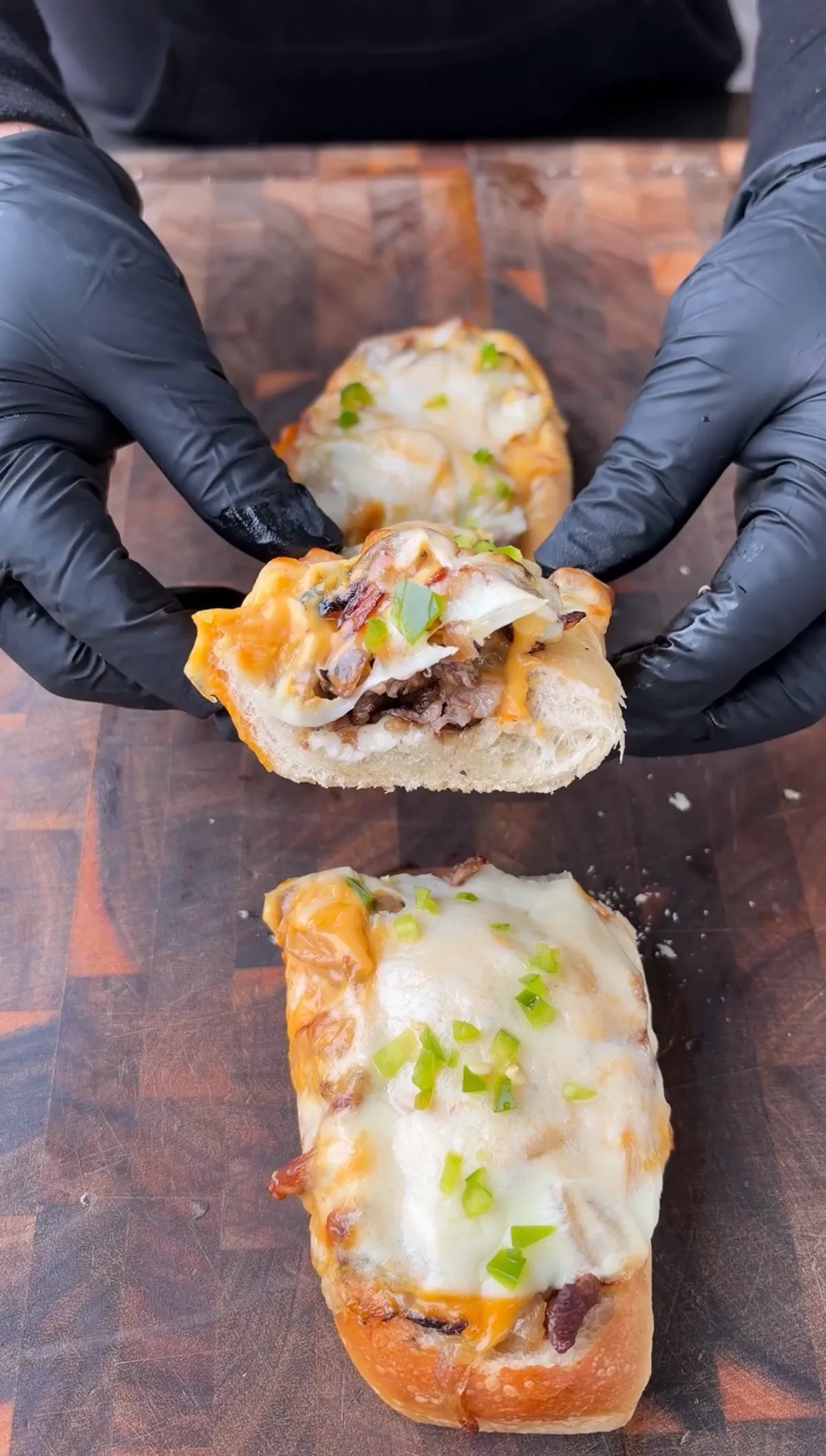 Gloved hands pulling apart a cheesesteak stuffed bread boat revealing ribeye, caramelized onions, and melted provolone