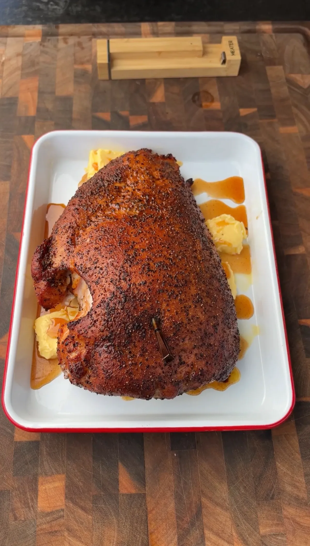 Cherrywood smoked turkey breast resting in honey butter on a white tray with a MEATER thermometer nearby