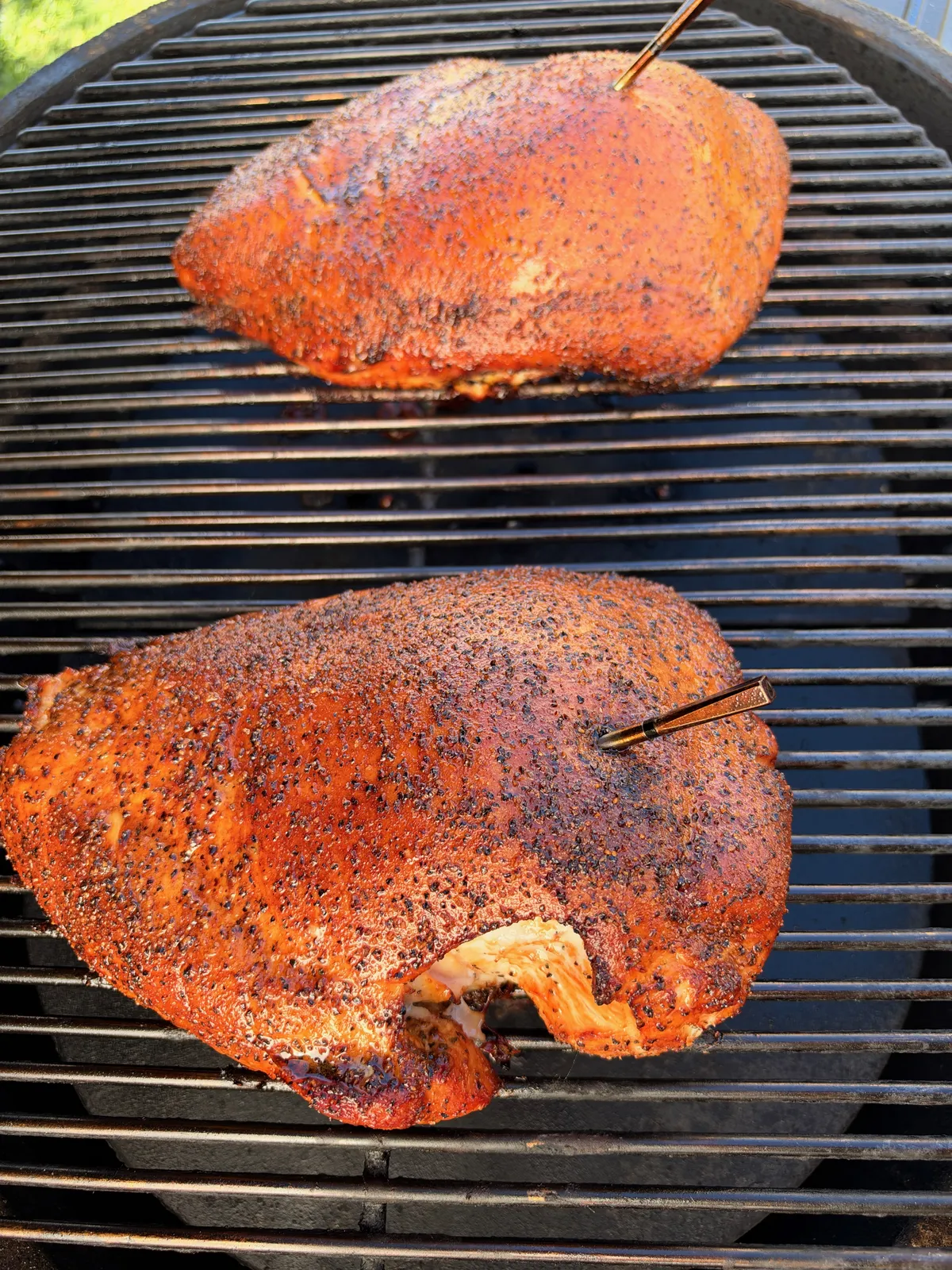 Two boneless turkey breasts with Texas-style salt, pepper, and garlic rub smoking on grill grates with cherrywood