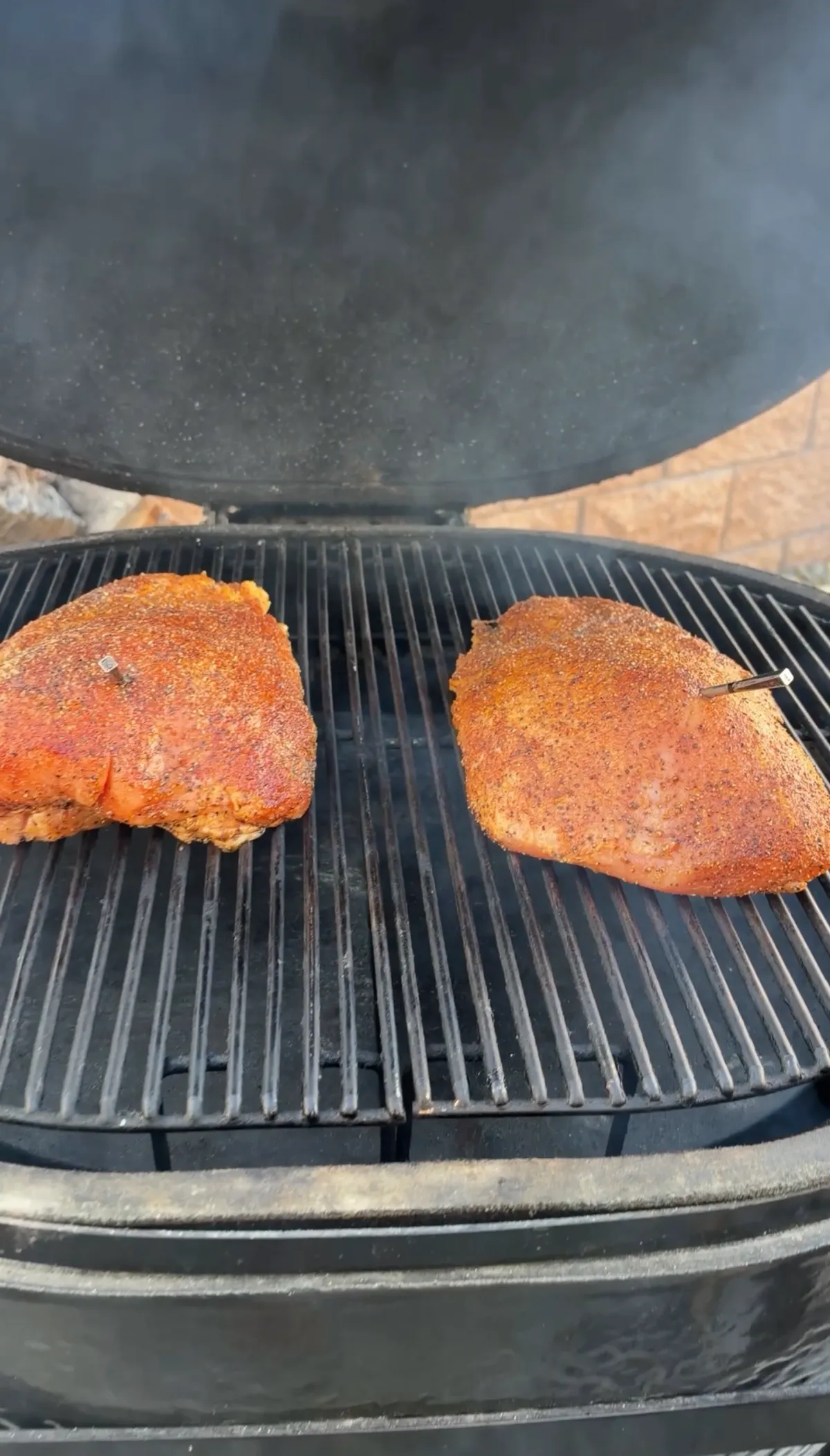 Two seasoned boneless turkey breasts with Texas-style rub smoking on grill grates with cherrywood smoke and meat probes inserted