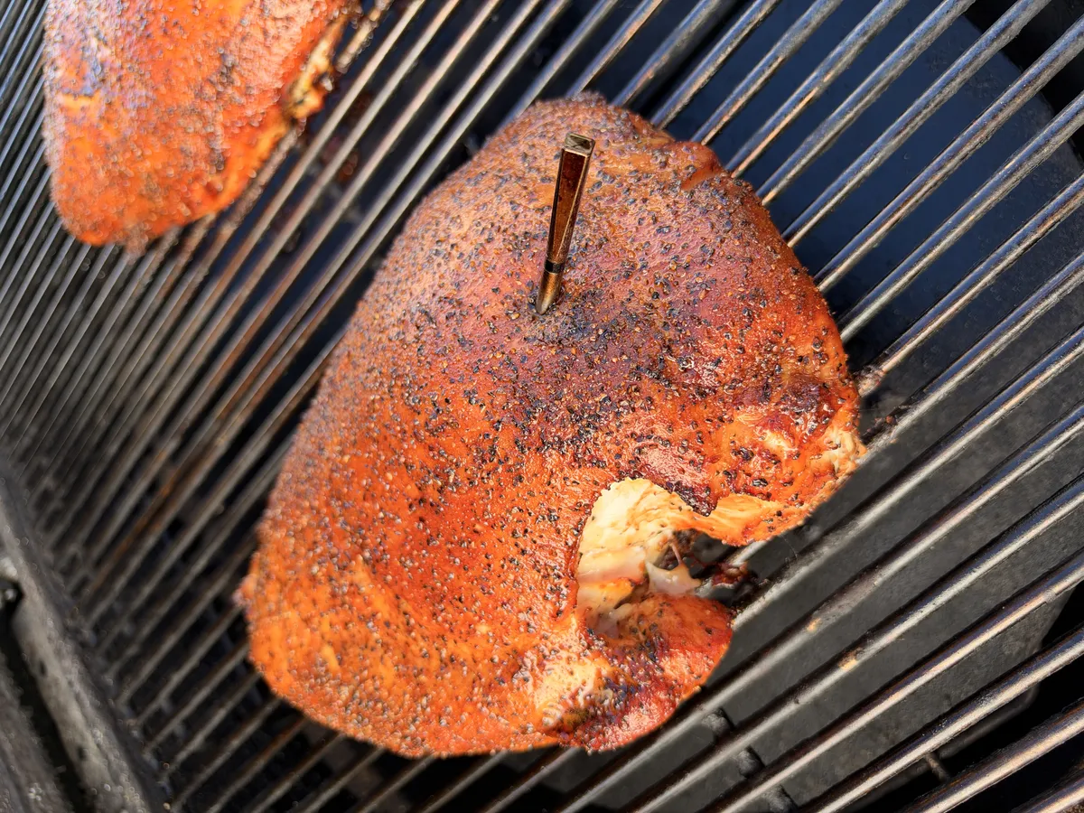 Boneless turkey breast with Texas-style salt, pepper, and garlic rub smoking on grates with a meat thermometer probe inserted