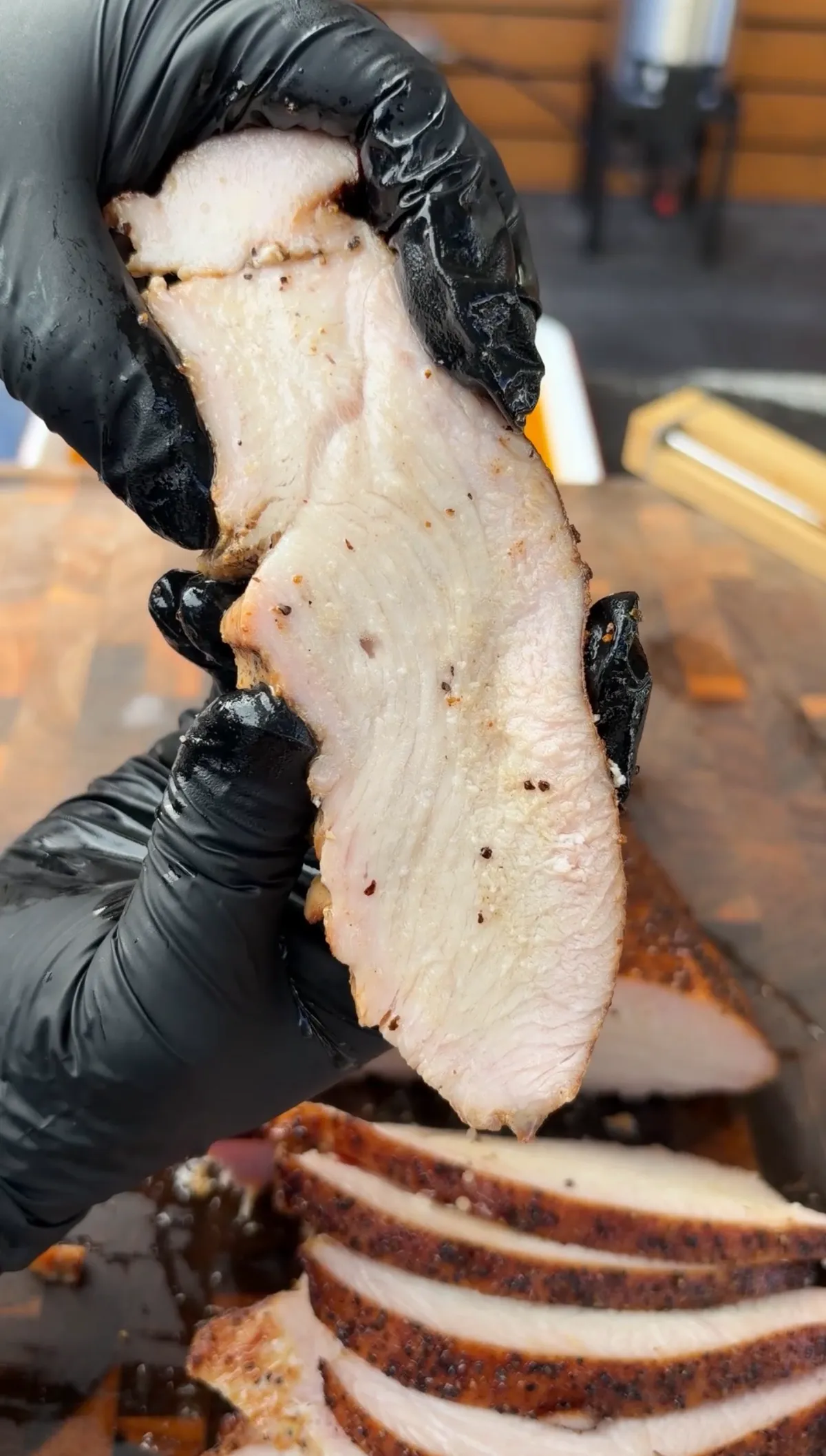 Sliced cherrywood smoked turkey breast held in black gloves, showing juicy interior with salt and pepper rub crust