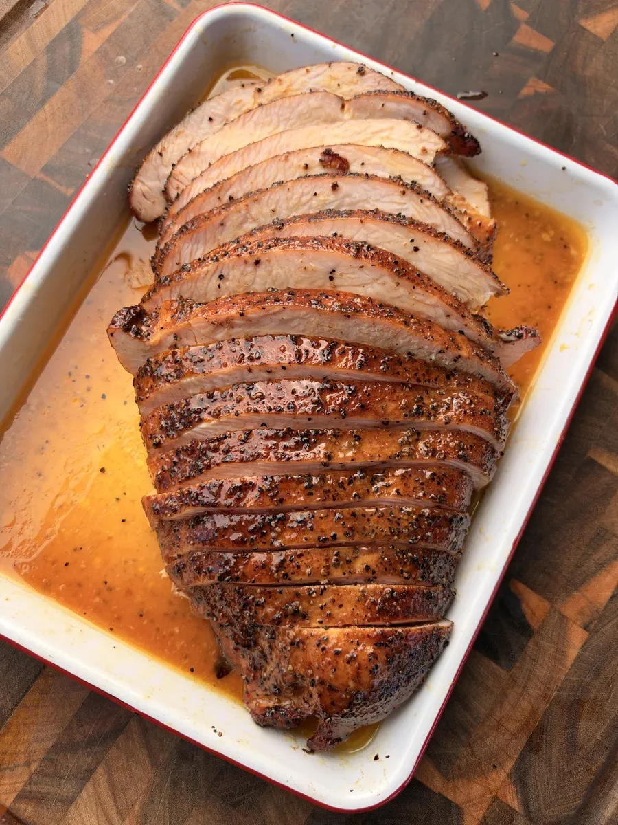 Sliced Texas-style cherrywood smoked turkey breast resting in melted honey butter in a white baking tray
