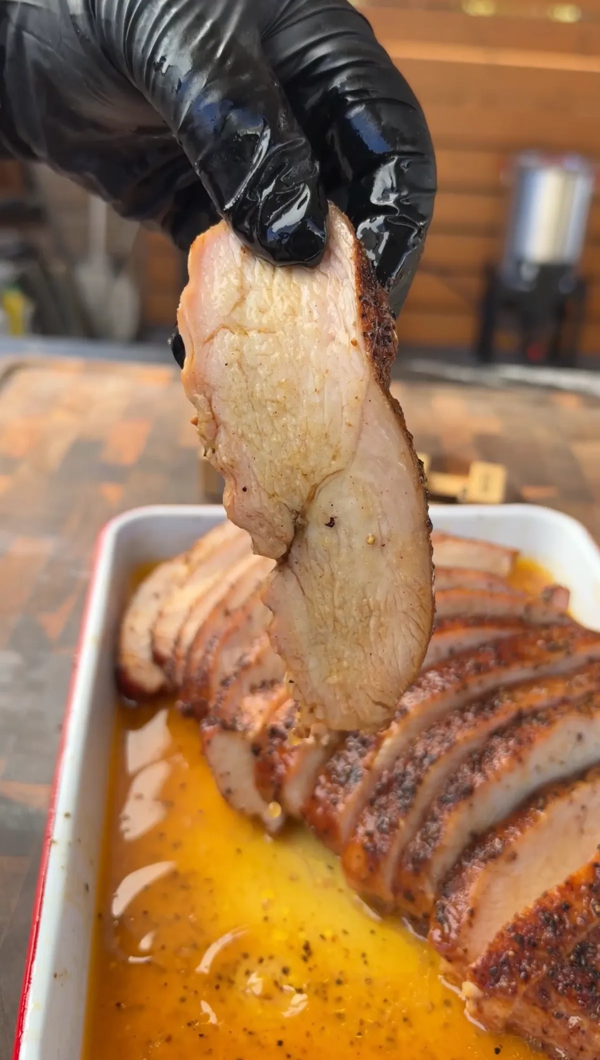 Gloved hand lifting a slice of cherrywood smoked turkey breast over a tray of melted honey butter juices