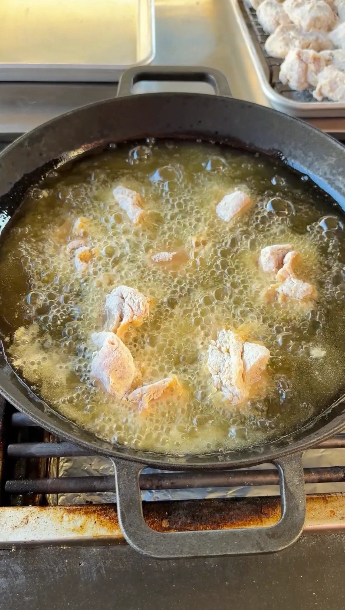 Flour-coated chicken thigh nuggets frying in bubbling hot oil in a cast iron skillet at 350°F
