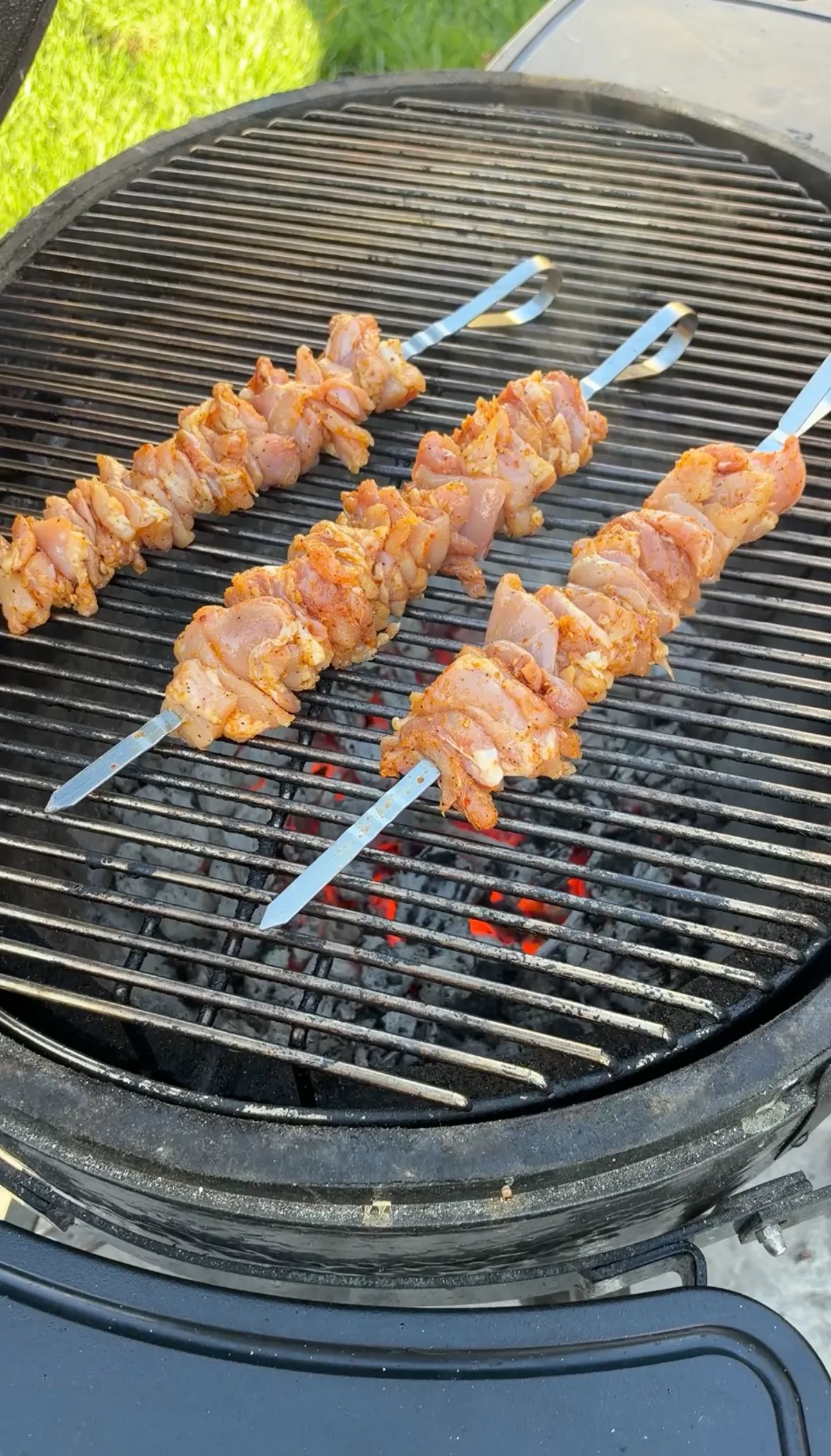 Seasoned chicken thigh skewers on metal skewers grilling over glowing charcoal on a charcoal grill